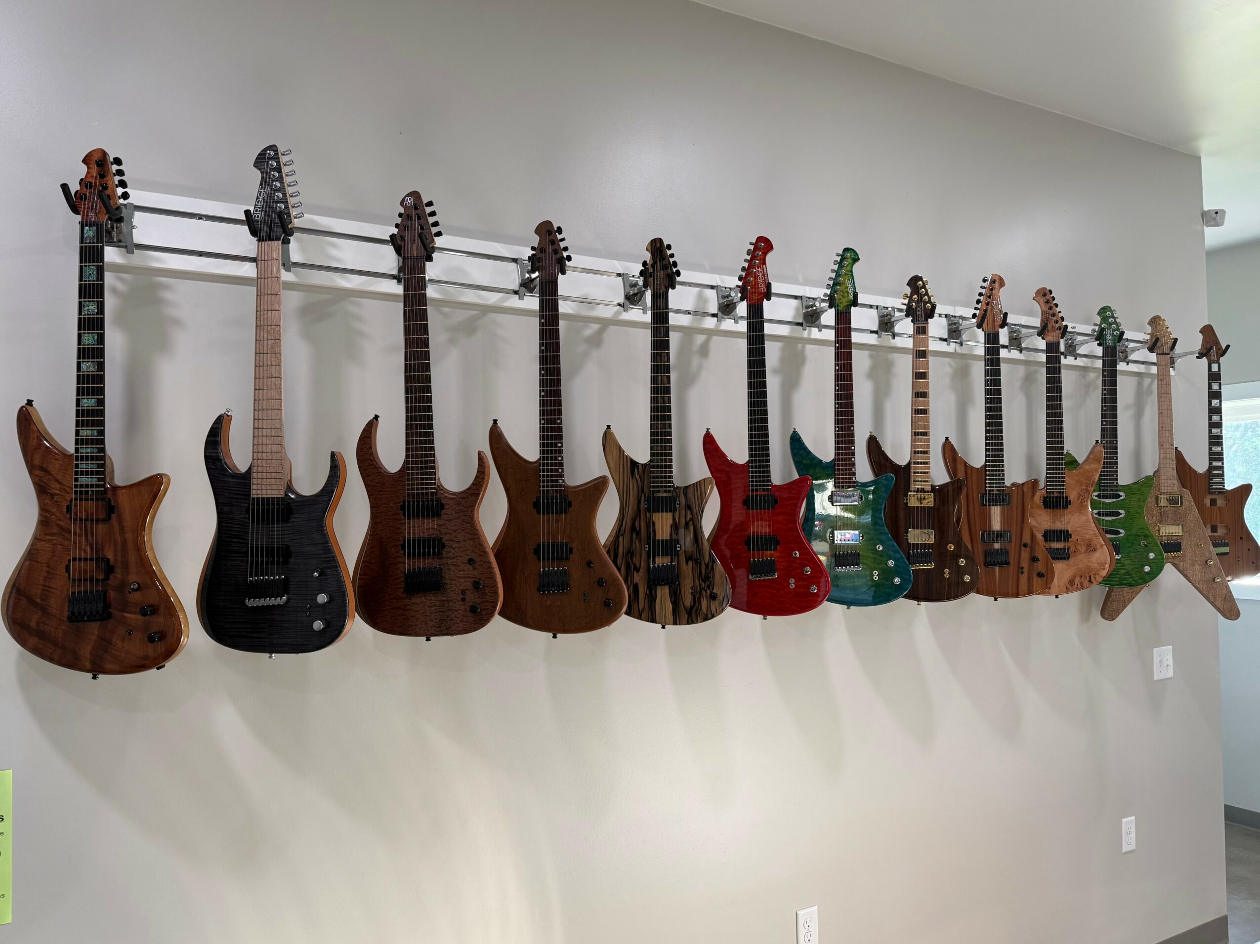 Multiple electric guitars hanging on a wall, arranged in a row, with various colors and designs.