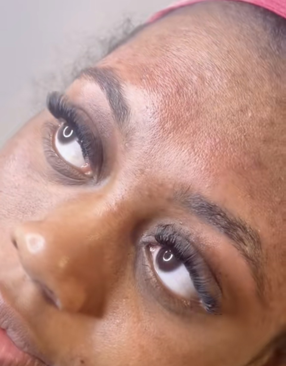 Close-up of a person's face with makeup, showing eyes, eyebrows, and forehead, tilted sideways.