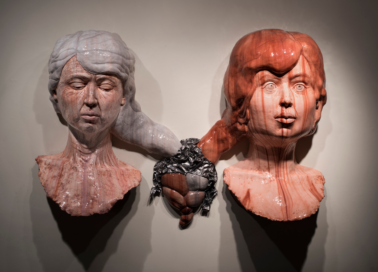 Two bust sculptures connected by a chain, one gray-haired woman and one red-haired girl, against a plain background.
