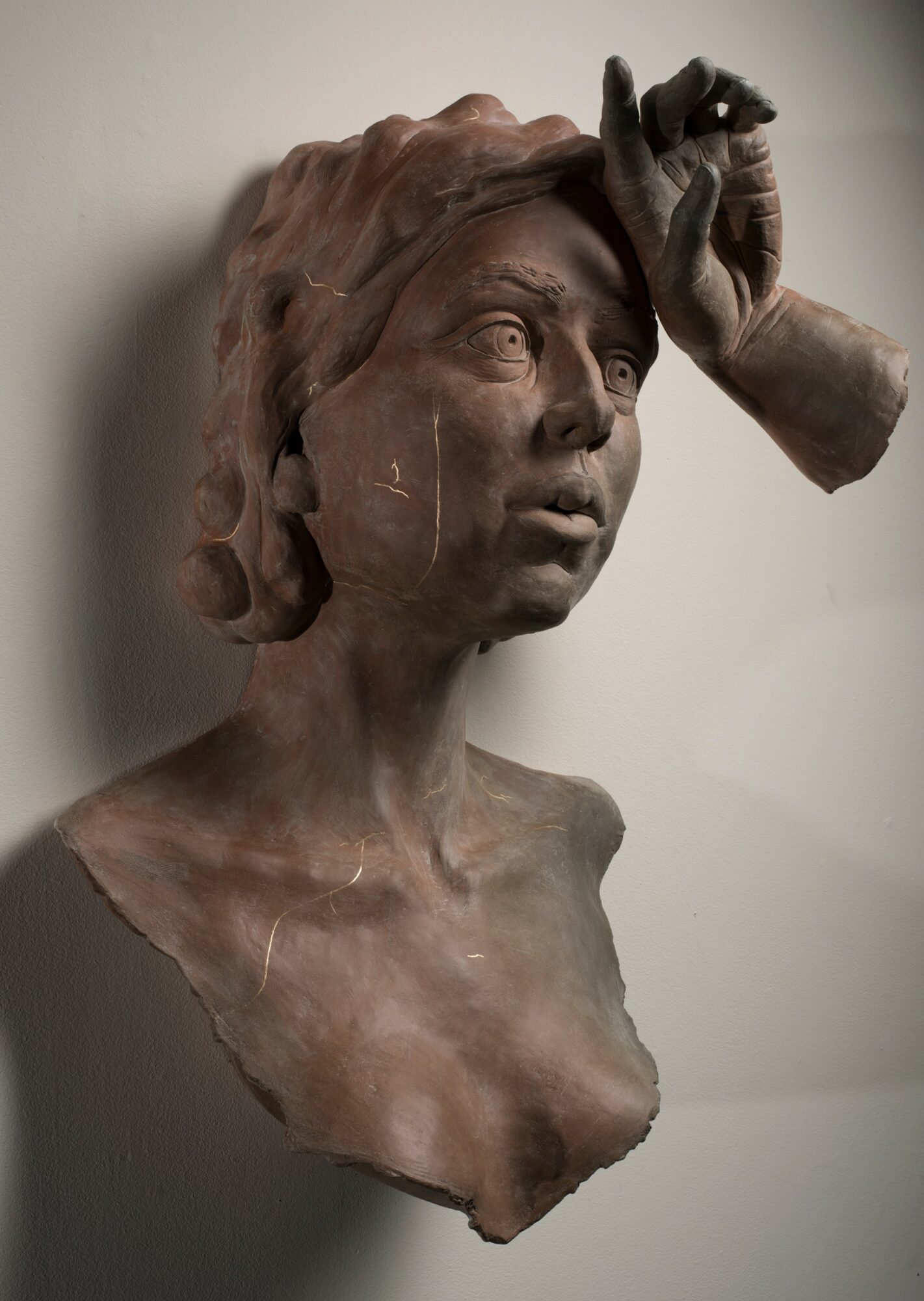 Clay sculpture of a woman with a hand on her forehead, detailed facial features, and wavy hair, against a plain background.