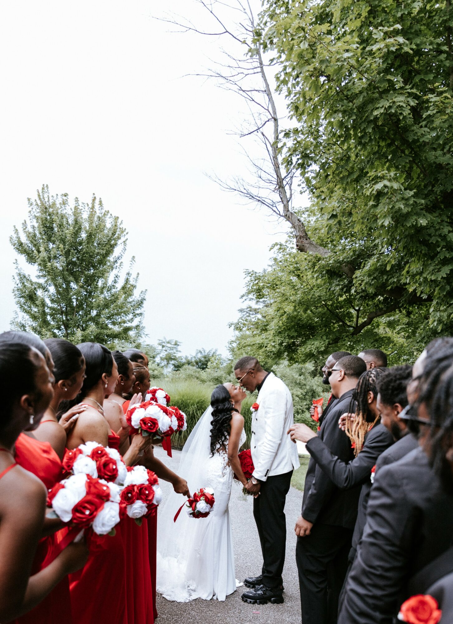Group of people outdoors, some in formal attire, participating in a ceremony with trees and sky in background.