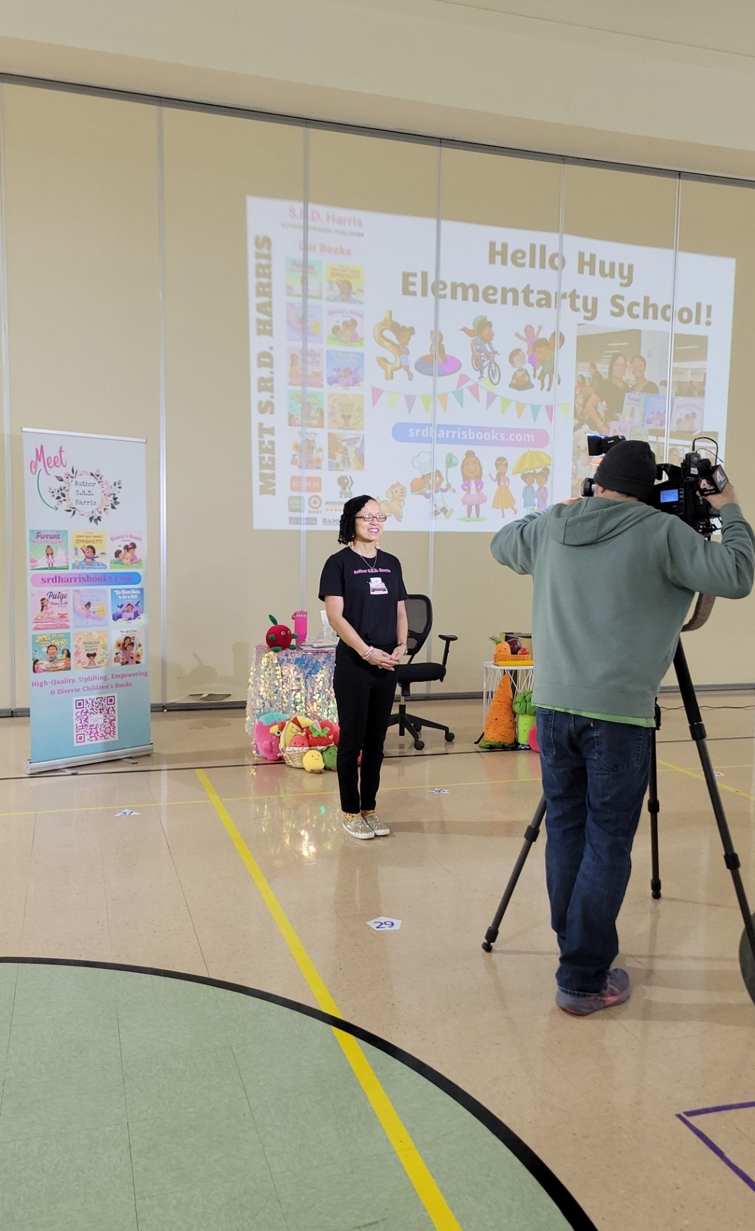 Person being interviewed by a camera operator in front of a school presentation screen, with colorful decorations nearby.