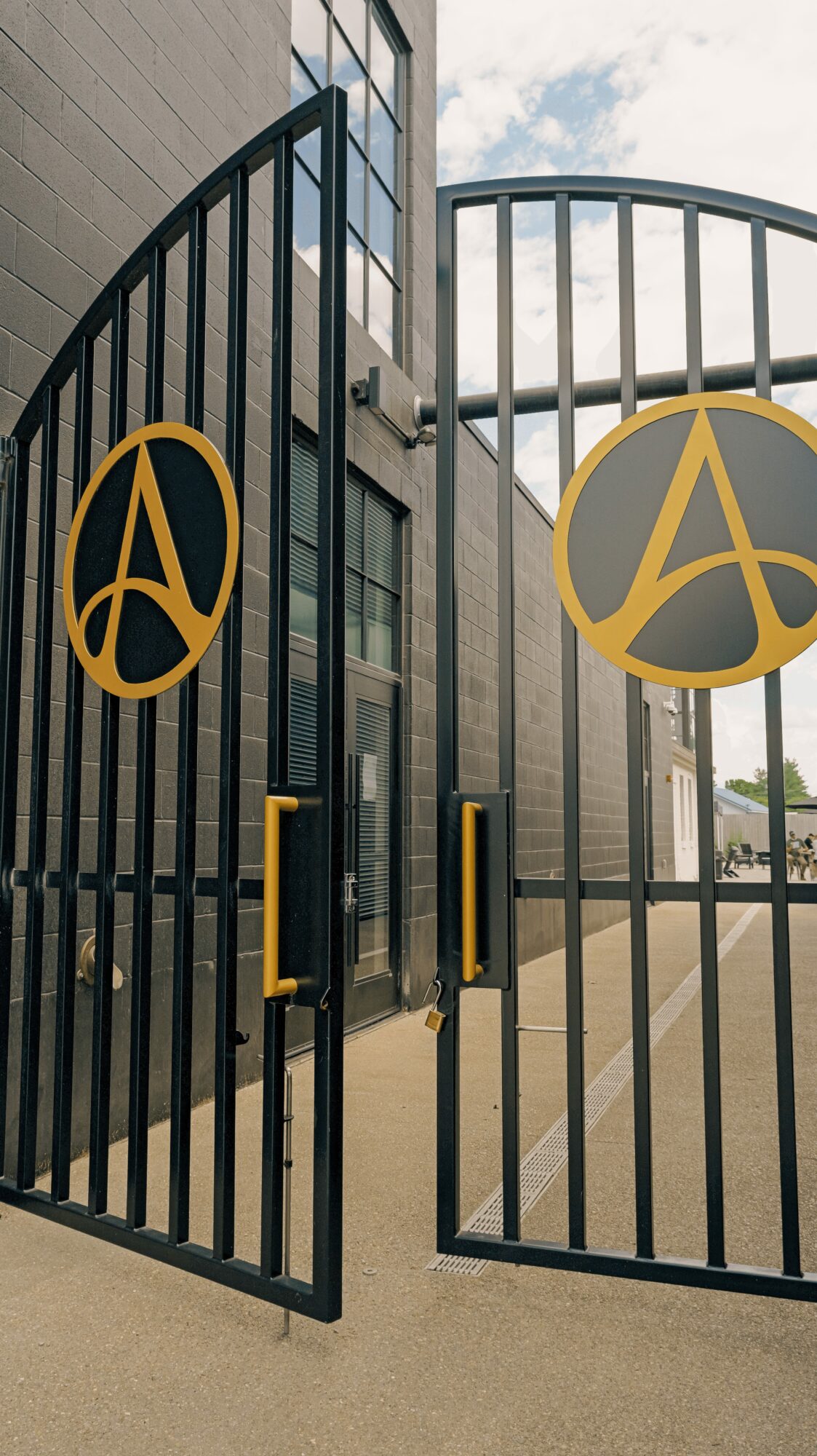 Black metal gate with gold circular logos, handles, and a building with windows in the background.