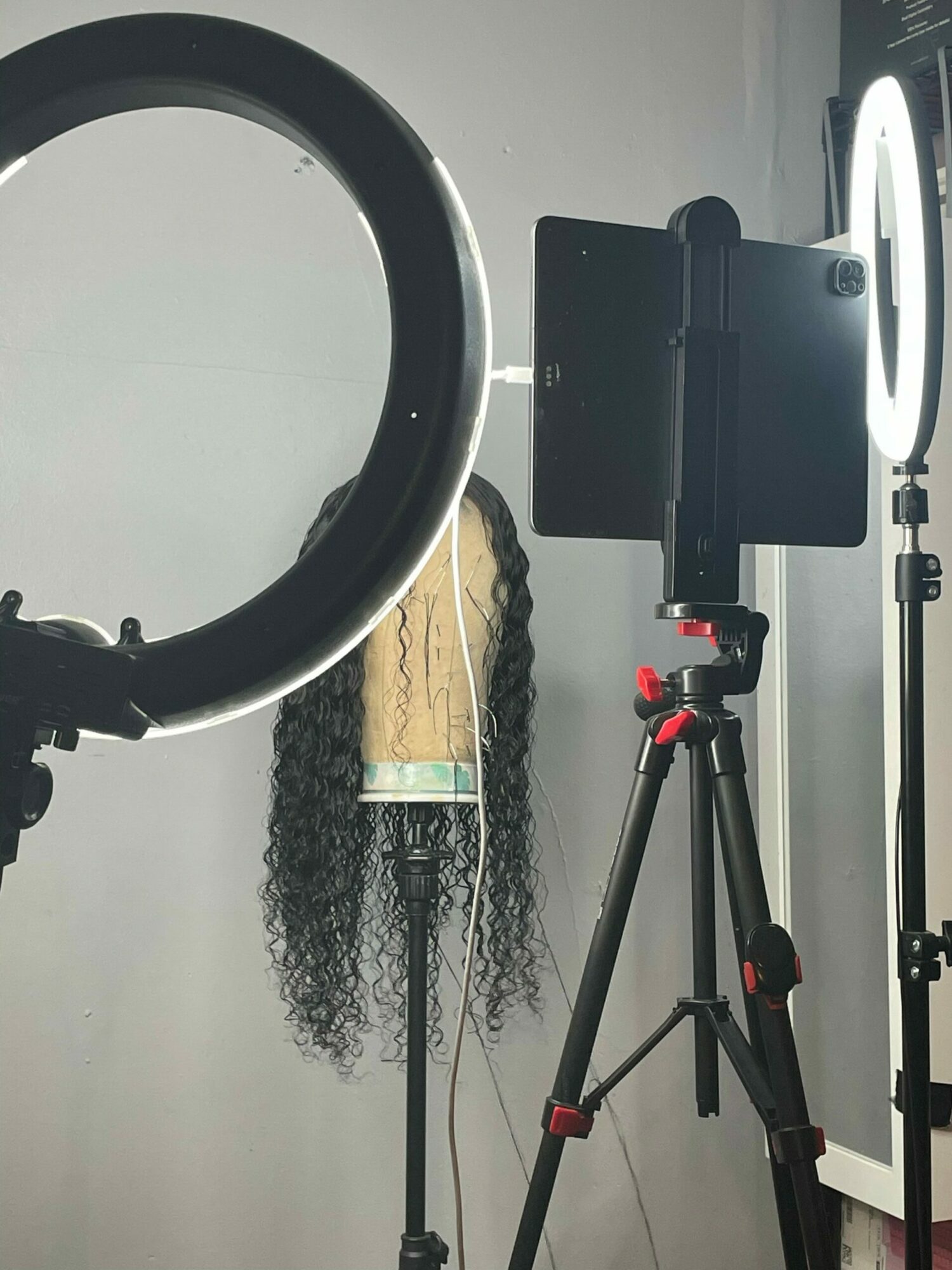 Camera mounted on a tripod, a mop with curly hair, and a black object on a gray wall.