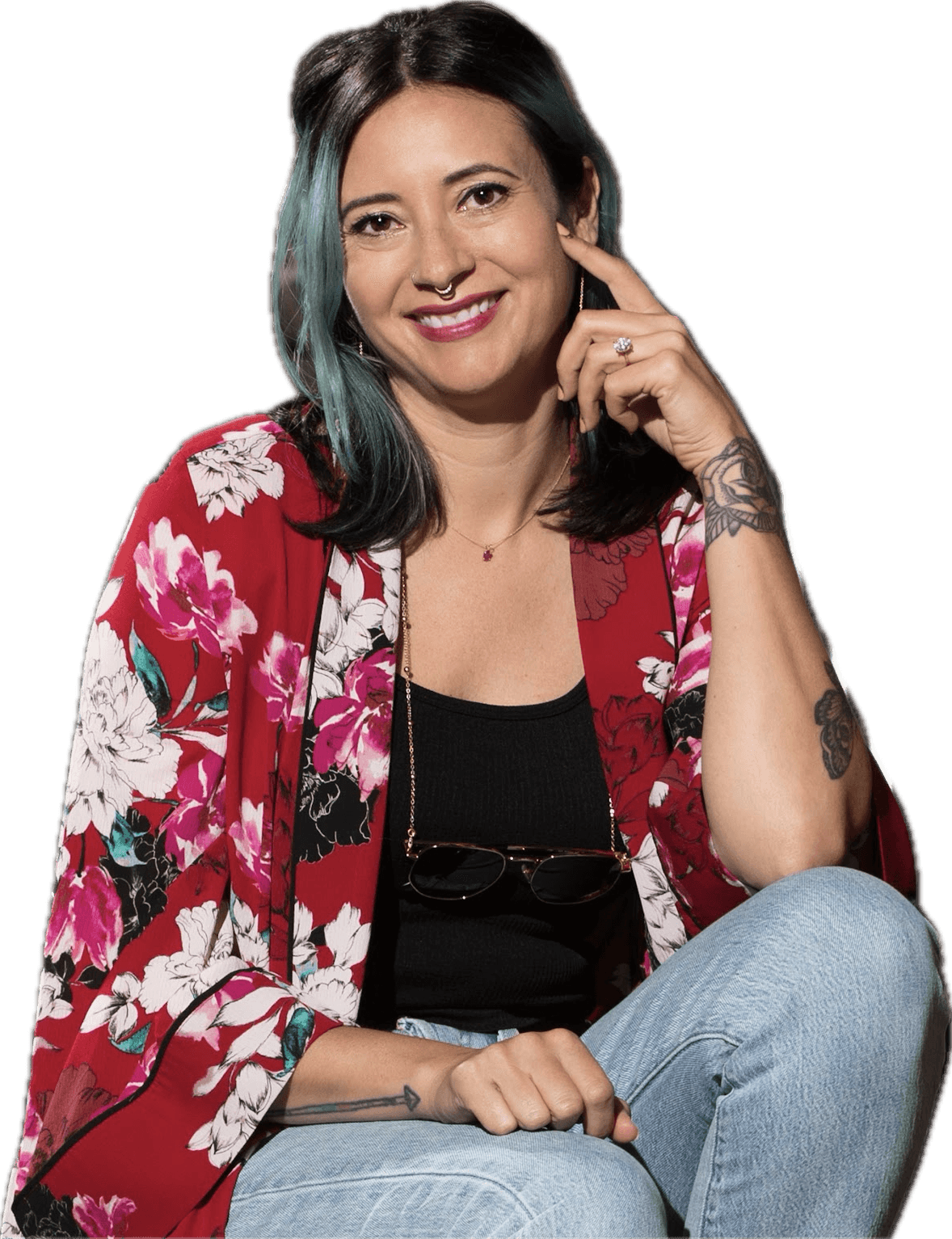 Woman with dark hair and a floral red jacket, smiling, sitting with her hand near her face, against a black background.
