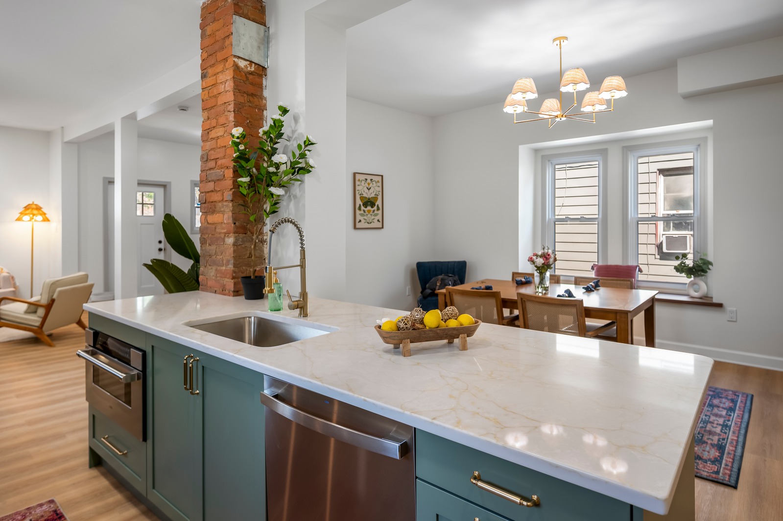 Modern kitchen with white island, blue cabinets, and a dining area with window, chandelier, and plants.