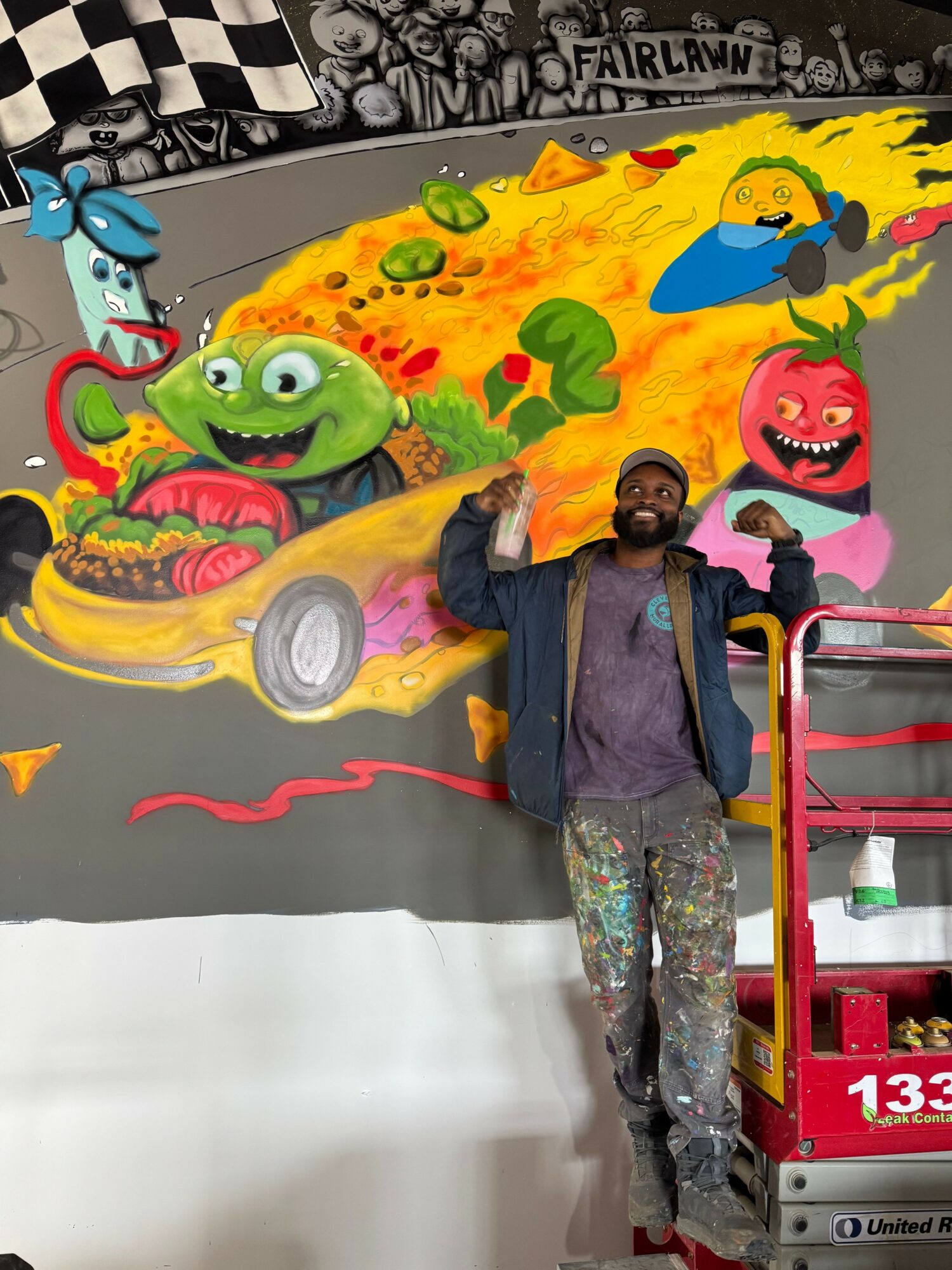 Person standing in front of colorful graffiti art with cartoon characters and abstract designs, holding a drink, in an indoor setting.