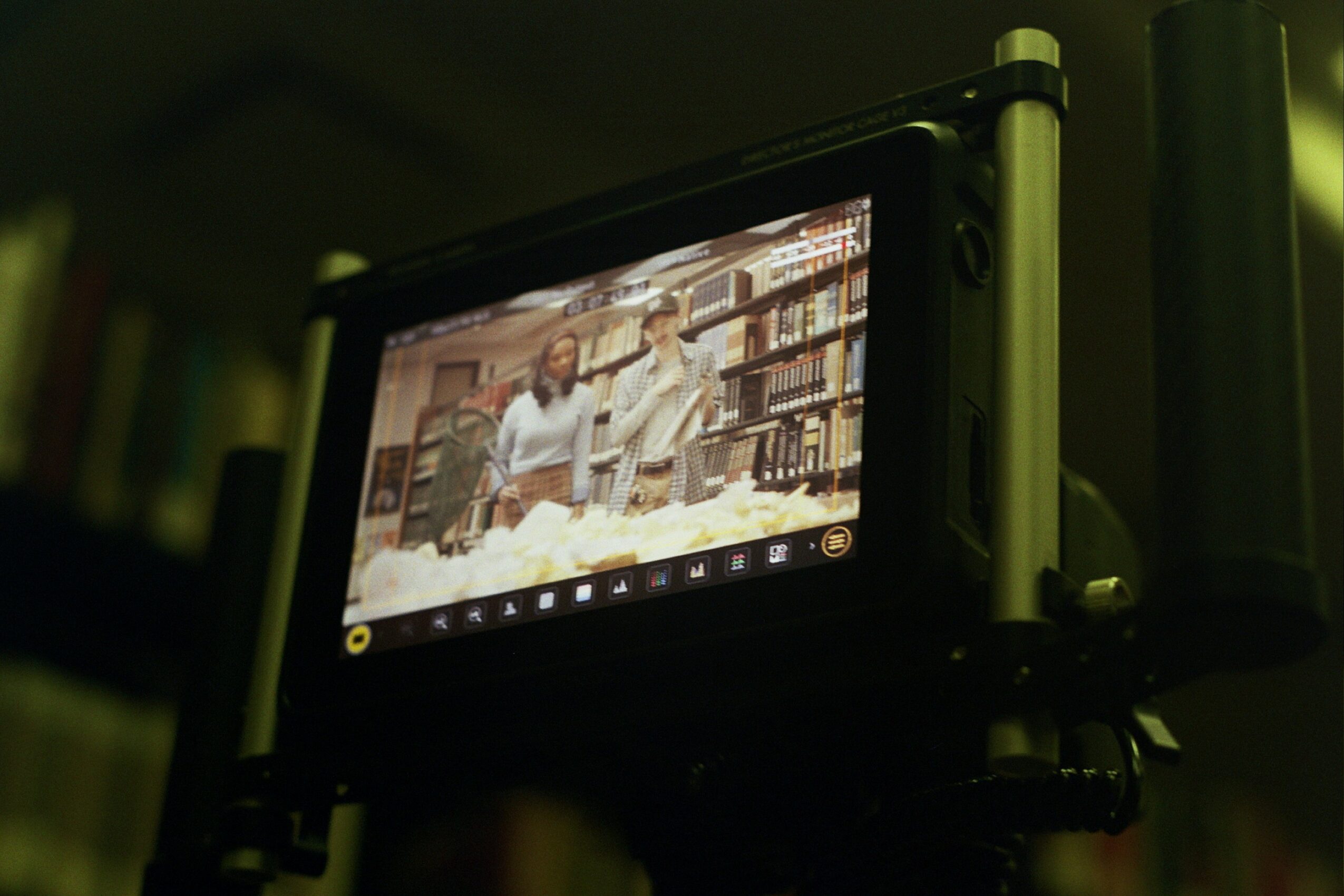 Screen displaying two people in a library or bookstore, surrounded by books, with a blurred background.