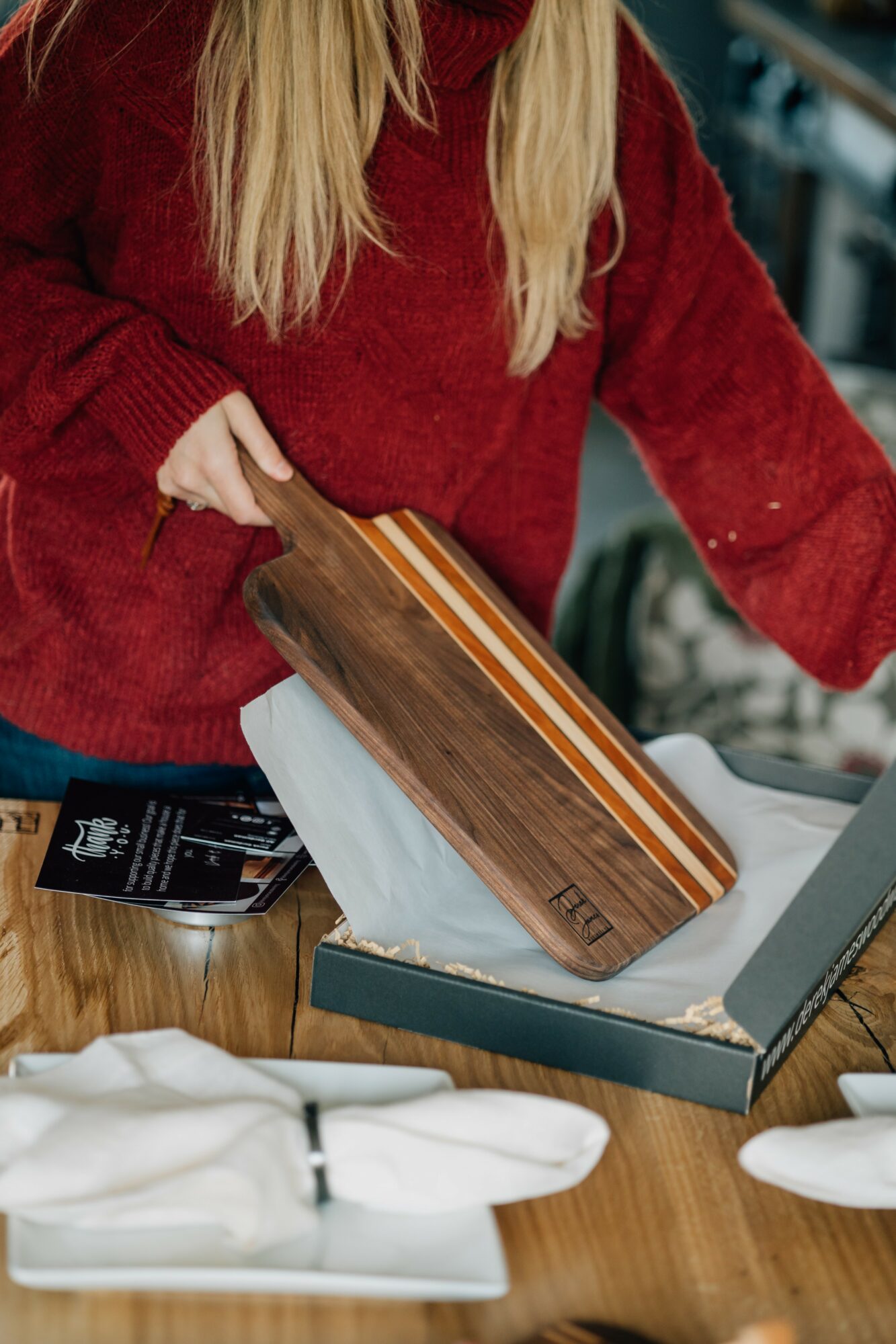 Person in red sweater holding a wooden cutting board over a table with packaging and white cloths.