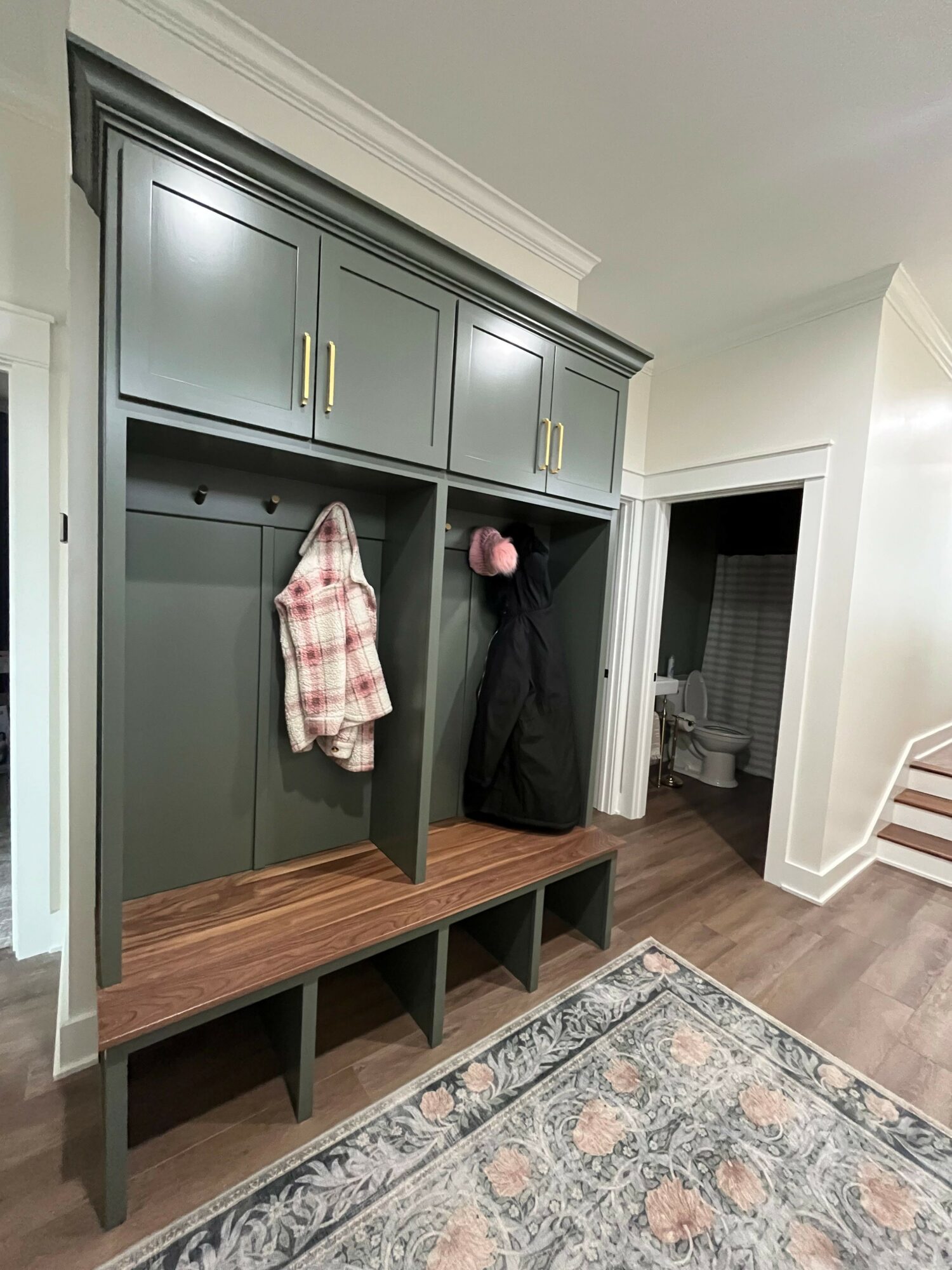 Gray cabinet with gold handles, a pink item, a plaid cloth, and open shelves in a room with a rug and hardwood floor.