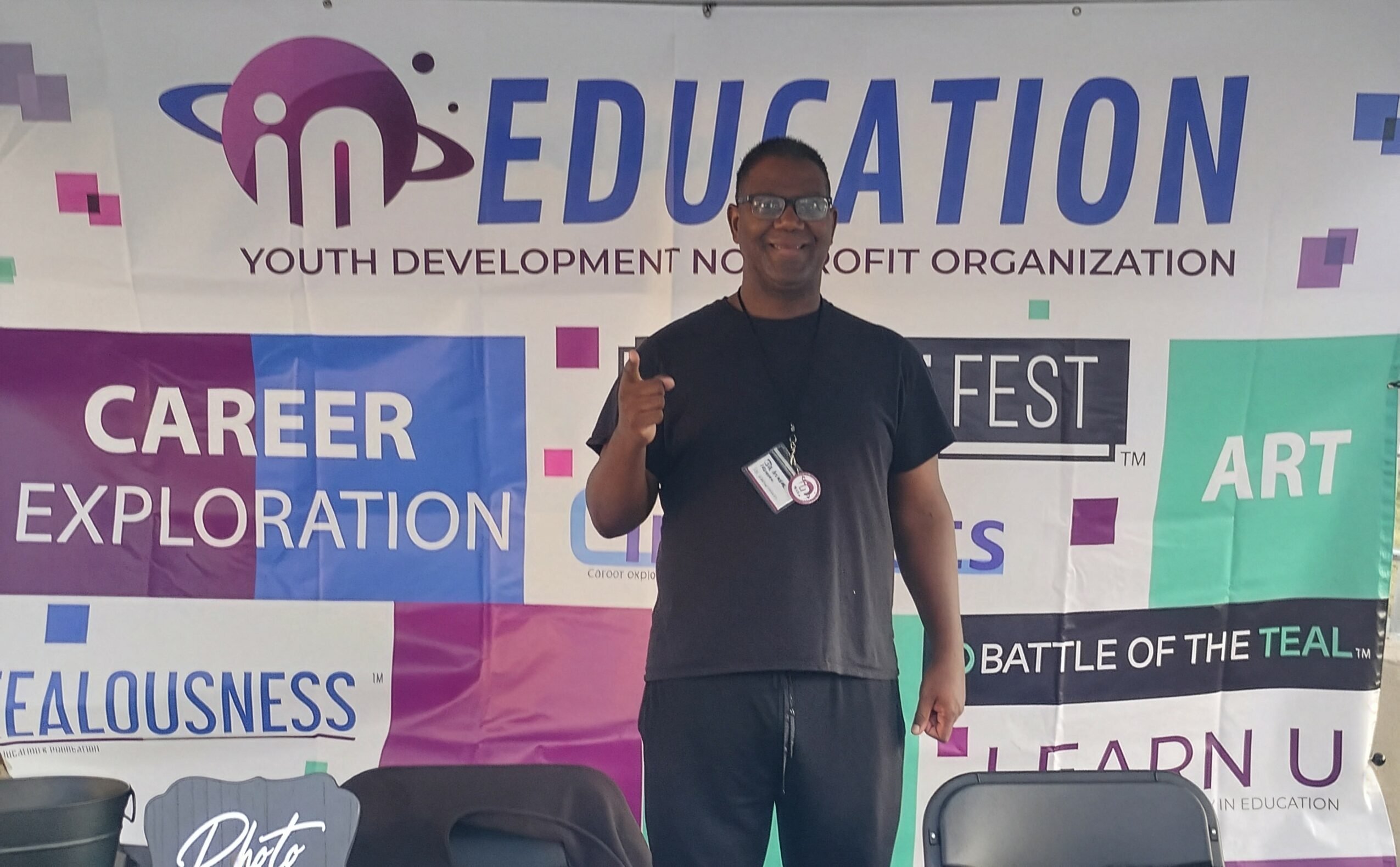 Young man standing in front of a colorful event banner, making a peace sign with his right hand.