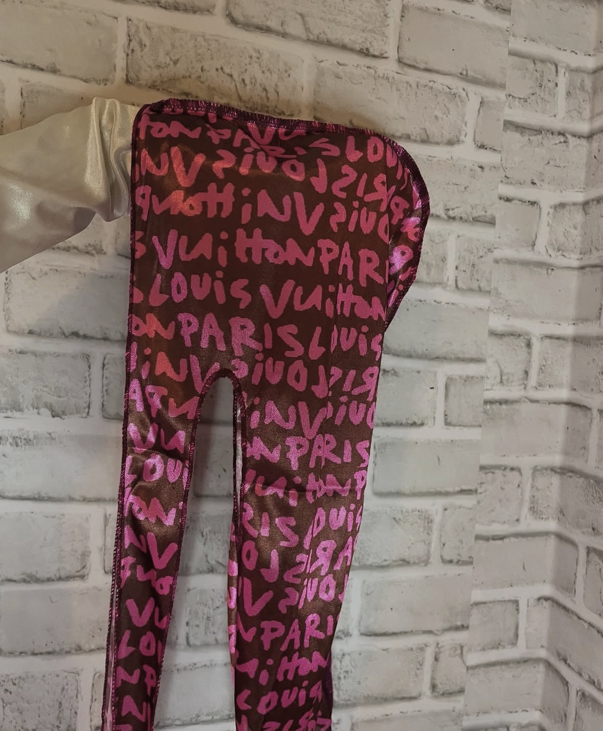 Person wearing pink and black patterned pants standing against a white brick wall.