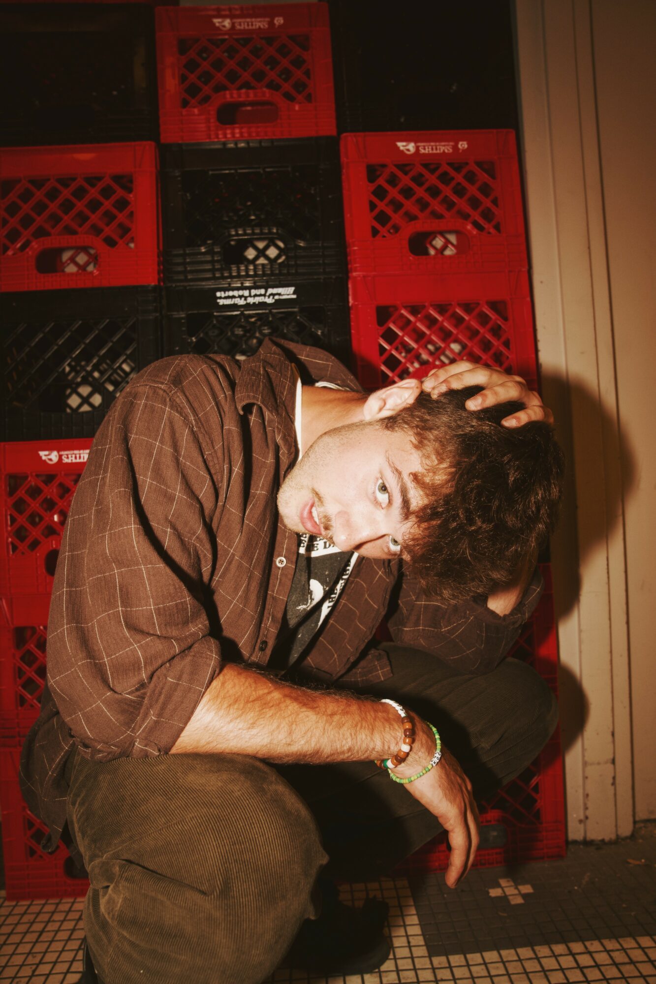 Person crouching with hand on head, surrounded by red and black crates, in a dimly lit setting.