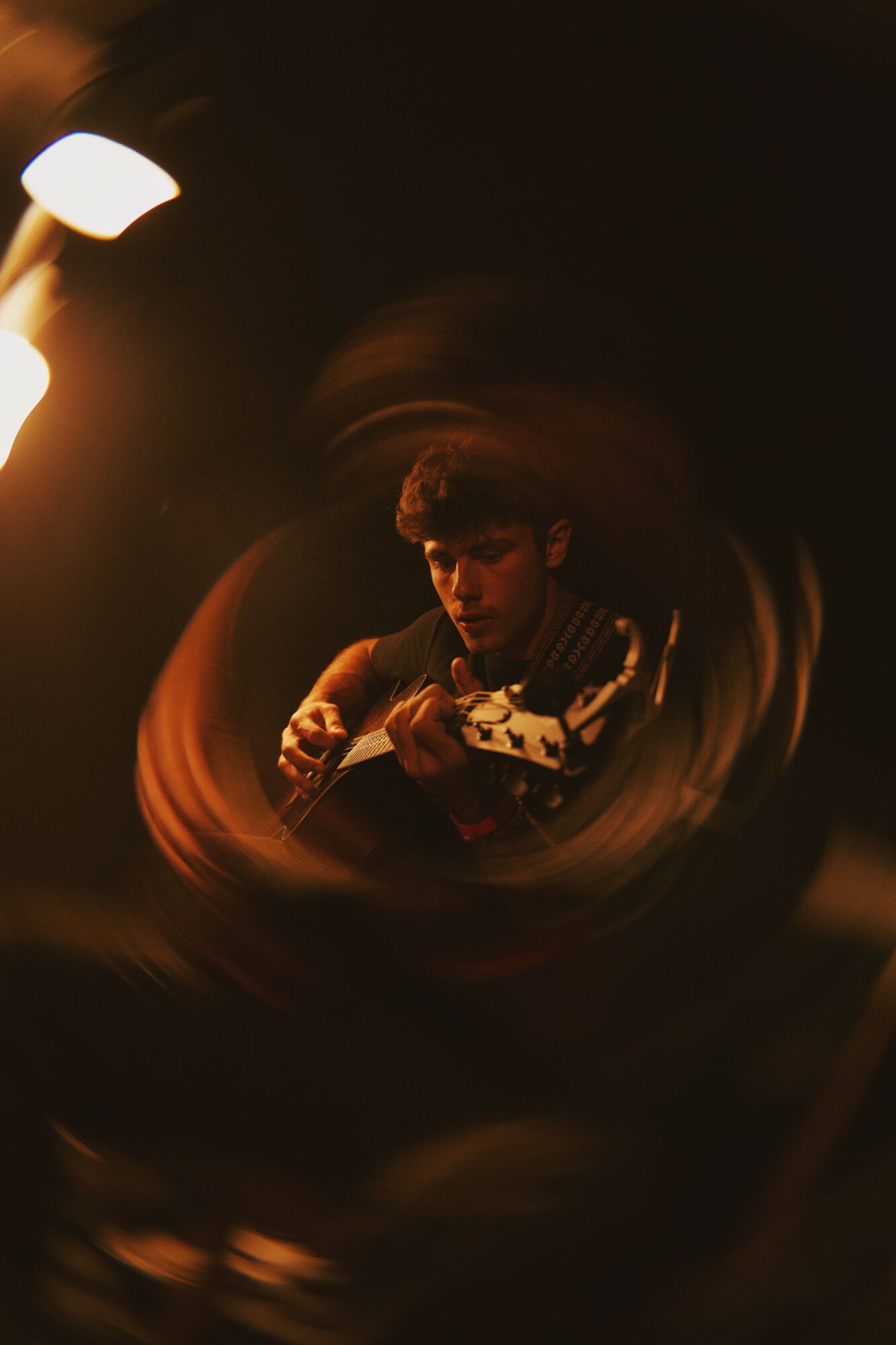 Person playing guitar in a dimly lit room with a warm light source, surrounded by swirling light effects.