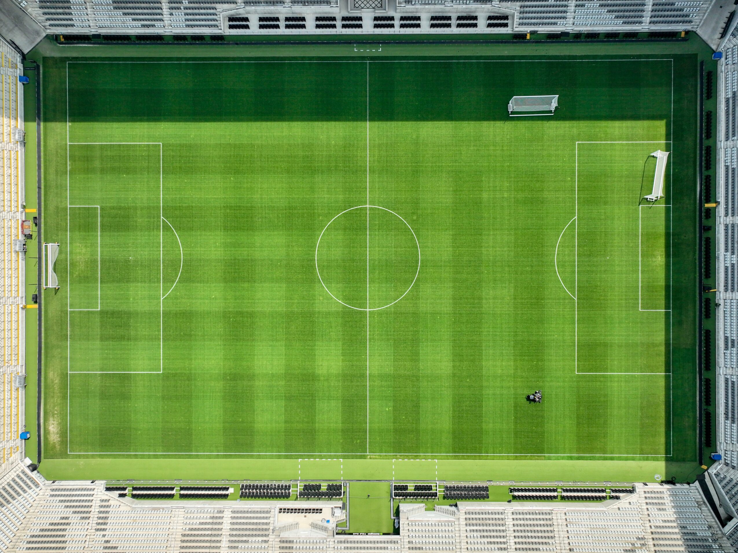 Aerial view of a soccer field with green grass, white lines, goalposts, and a ball near the penalty area.