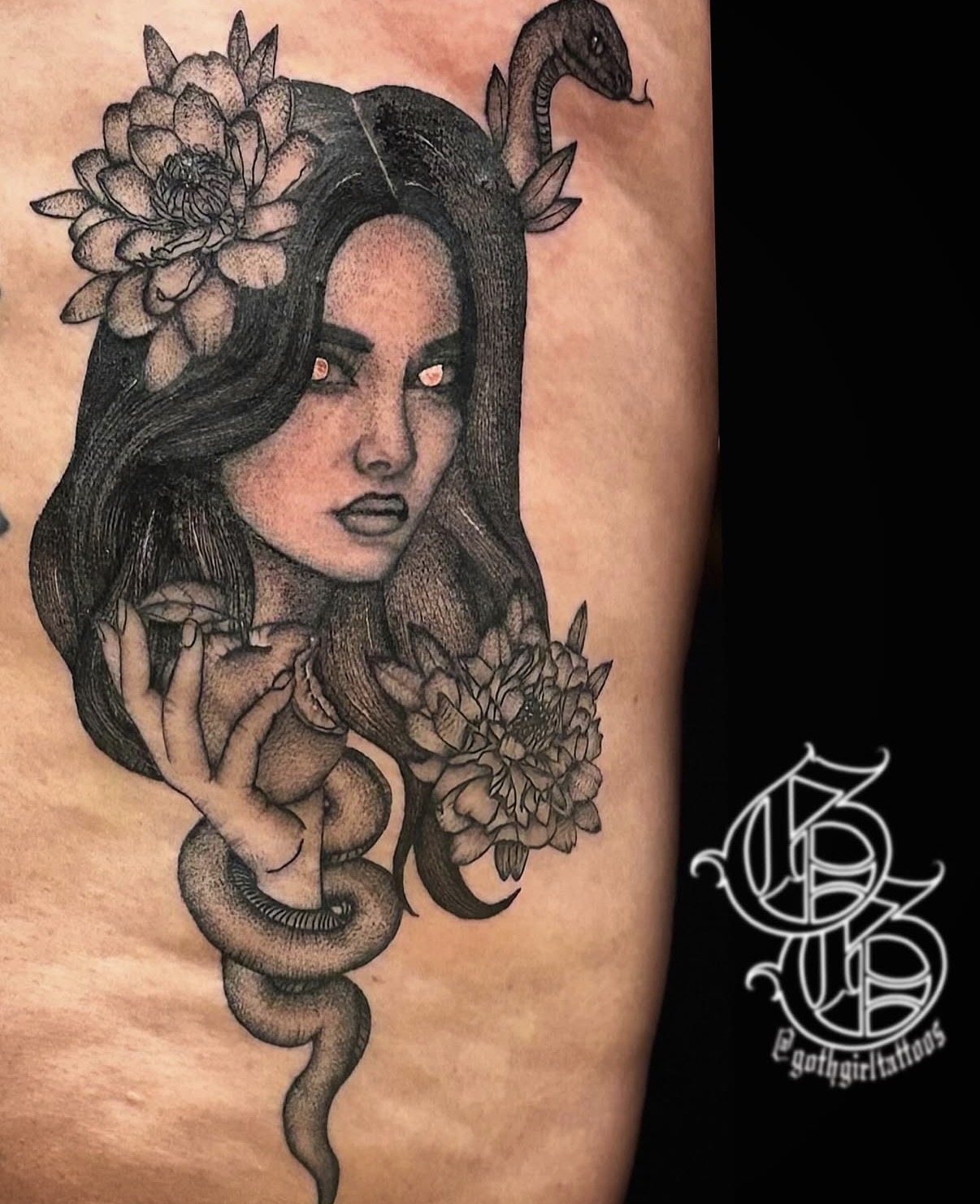 Black and gray tattoo of a woman with flowers and a snake on her head and shoulder, detailed shading, on skin.