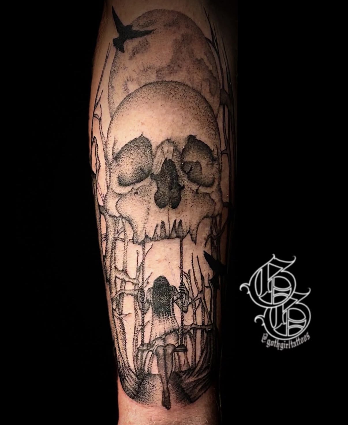 Tattoo of a skull with a moon and bird, with trees and a spider below, in black and gray ink.