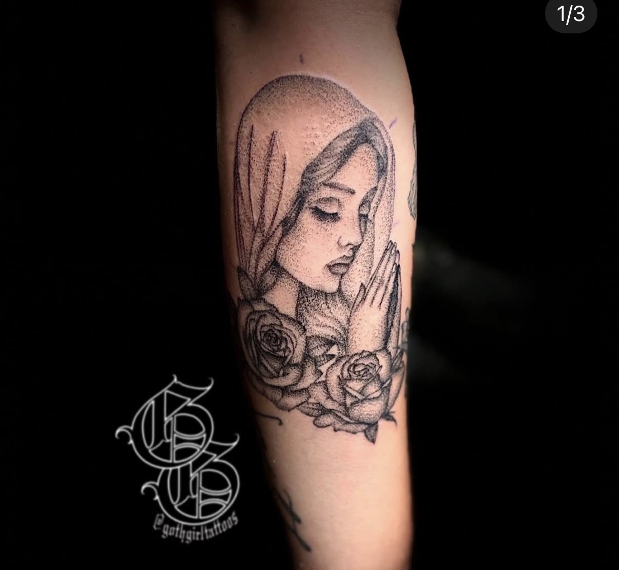 Tattoo of a woman's face with closed eyes, hands in prayer, surrounded by roses, on arm, black ink, detailed line art.