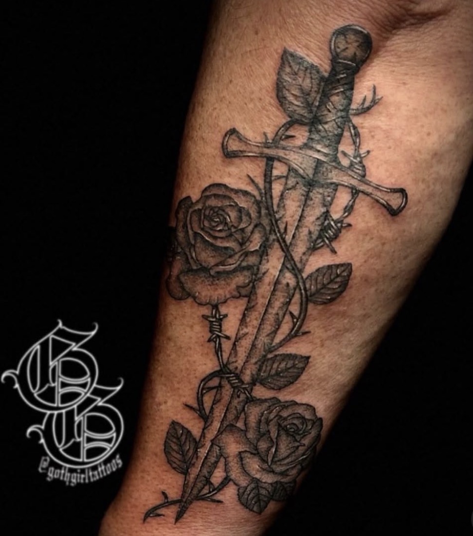 Tattoo of a sword intertwined with a rose and leaves on a person's arm.