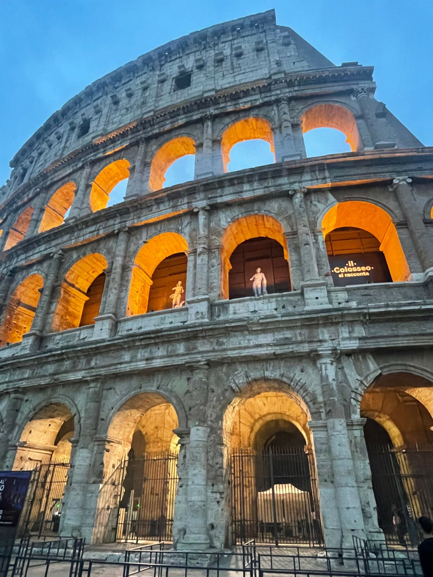 The Colosseum illuminated at night with arches and stone structure visible.