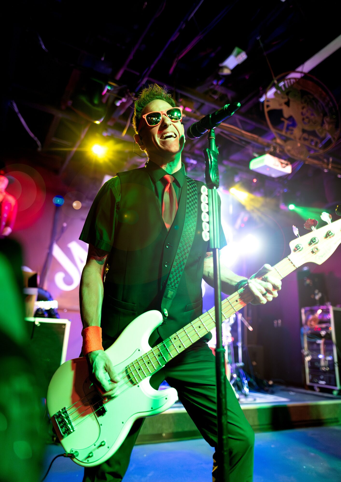 Musician with sunglasses and a guitar performing on stage with colorful lights.