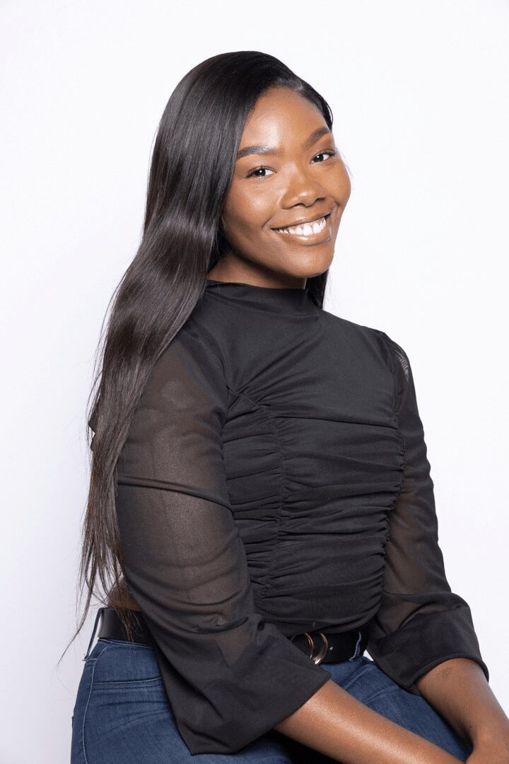 Young woman with long, straight hair smiling, wearing a black top and blue jeans, against a white background.