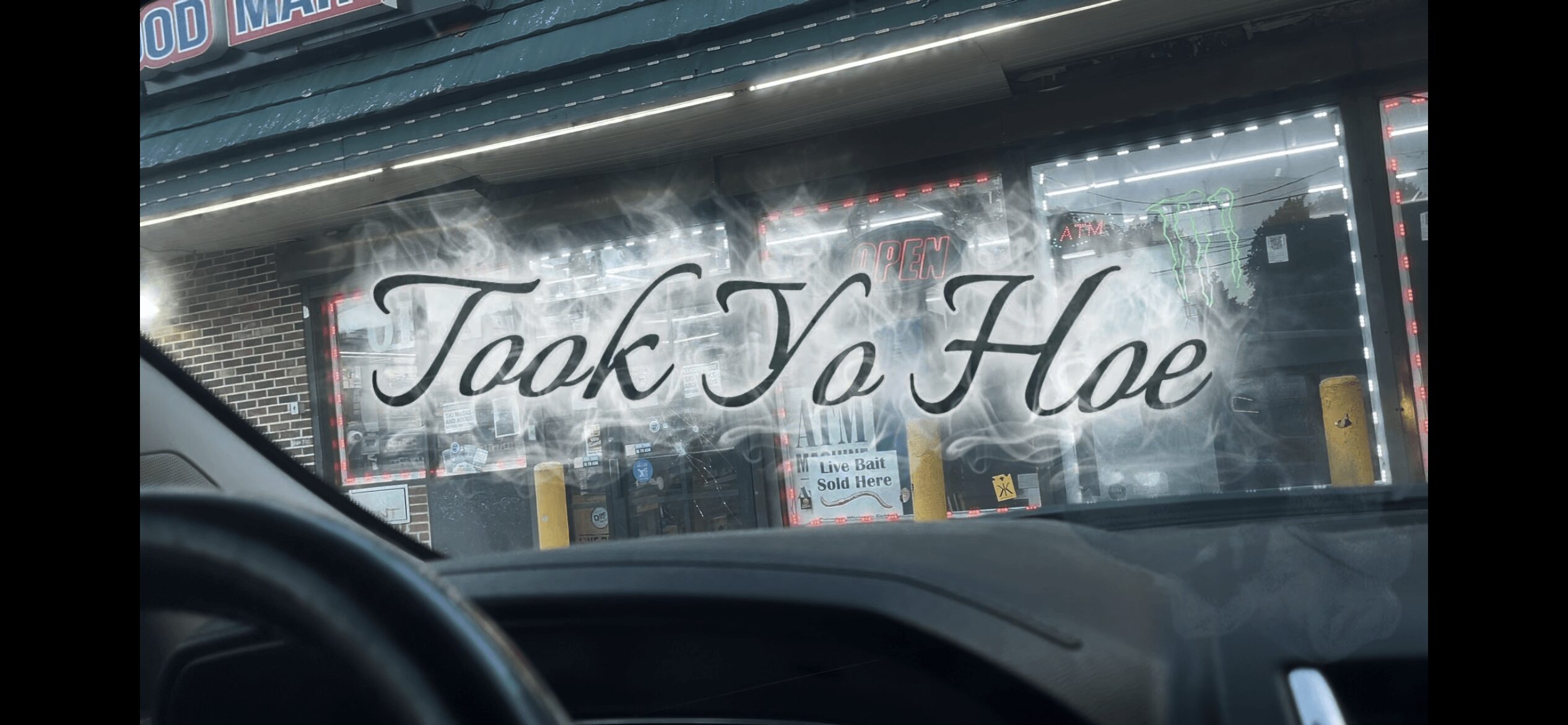 View through a car windshield showing a sign with the text 'Took Yo Hae' in cursive, outside a store.