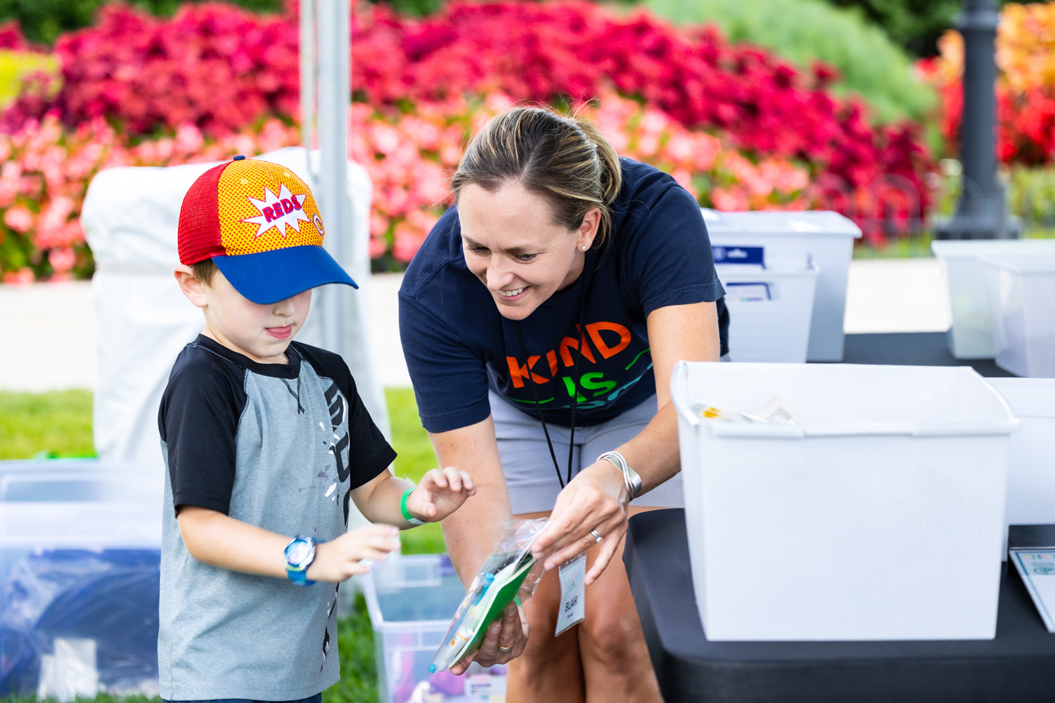 Woman and child smiling outdoors, woman showing a book to the child, colorful flowers in background