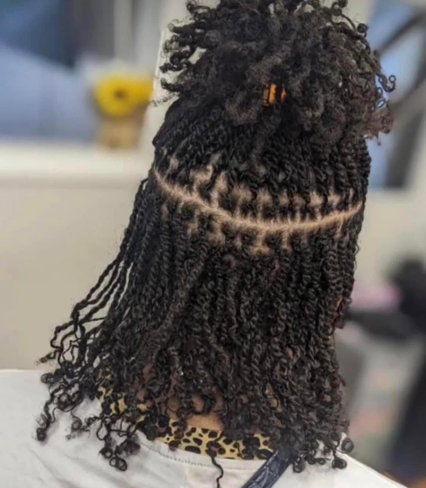 Person with styled dreadlocks and a high bun, facing away, in a room with blurred background.