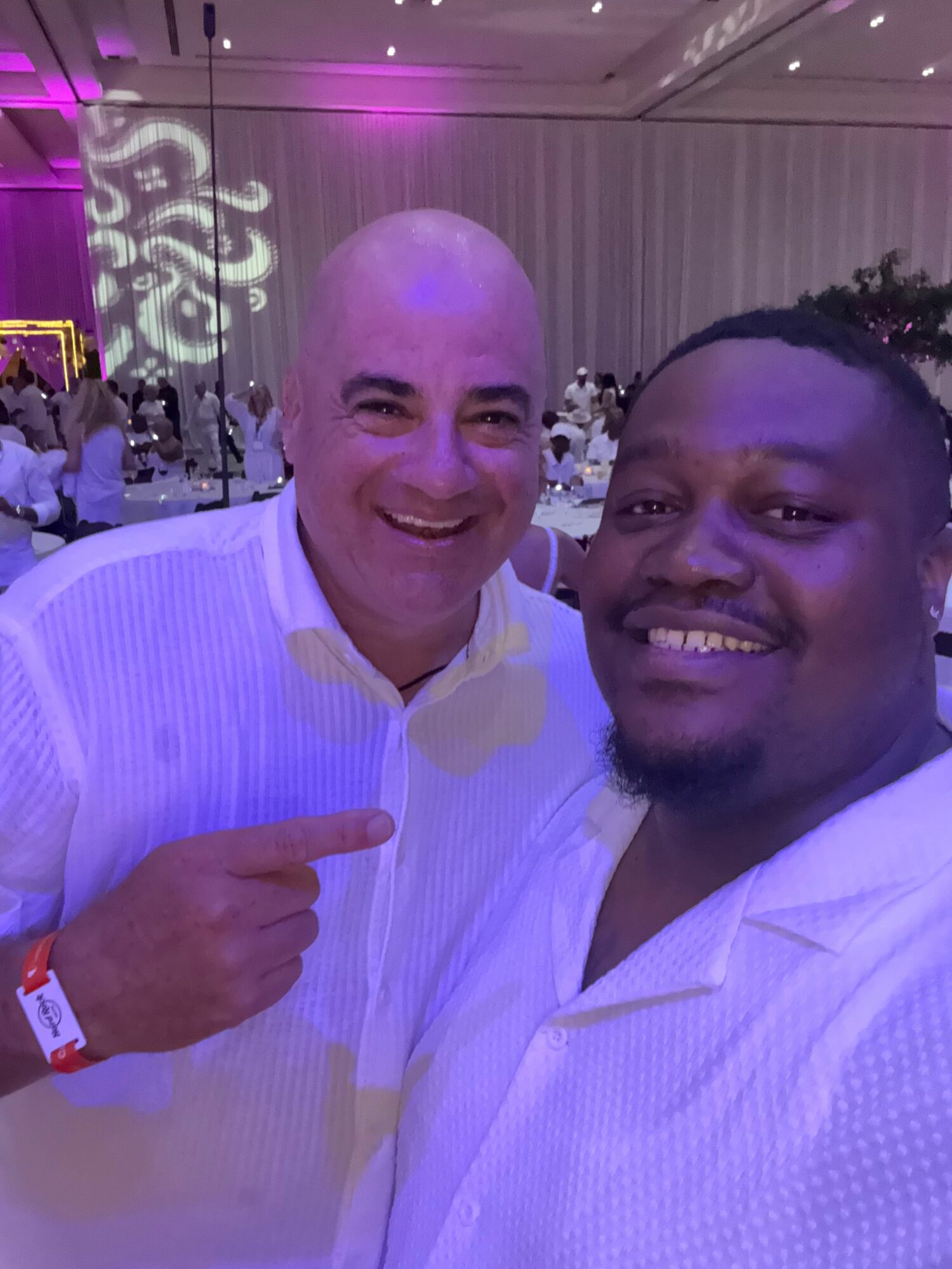 Two men smiling, one with a shaved head and the other with short hair, in a decorated indoor setting.