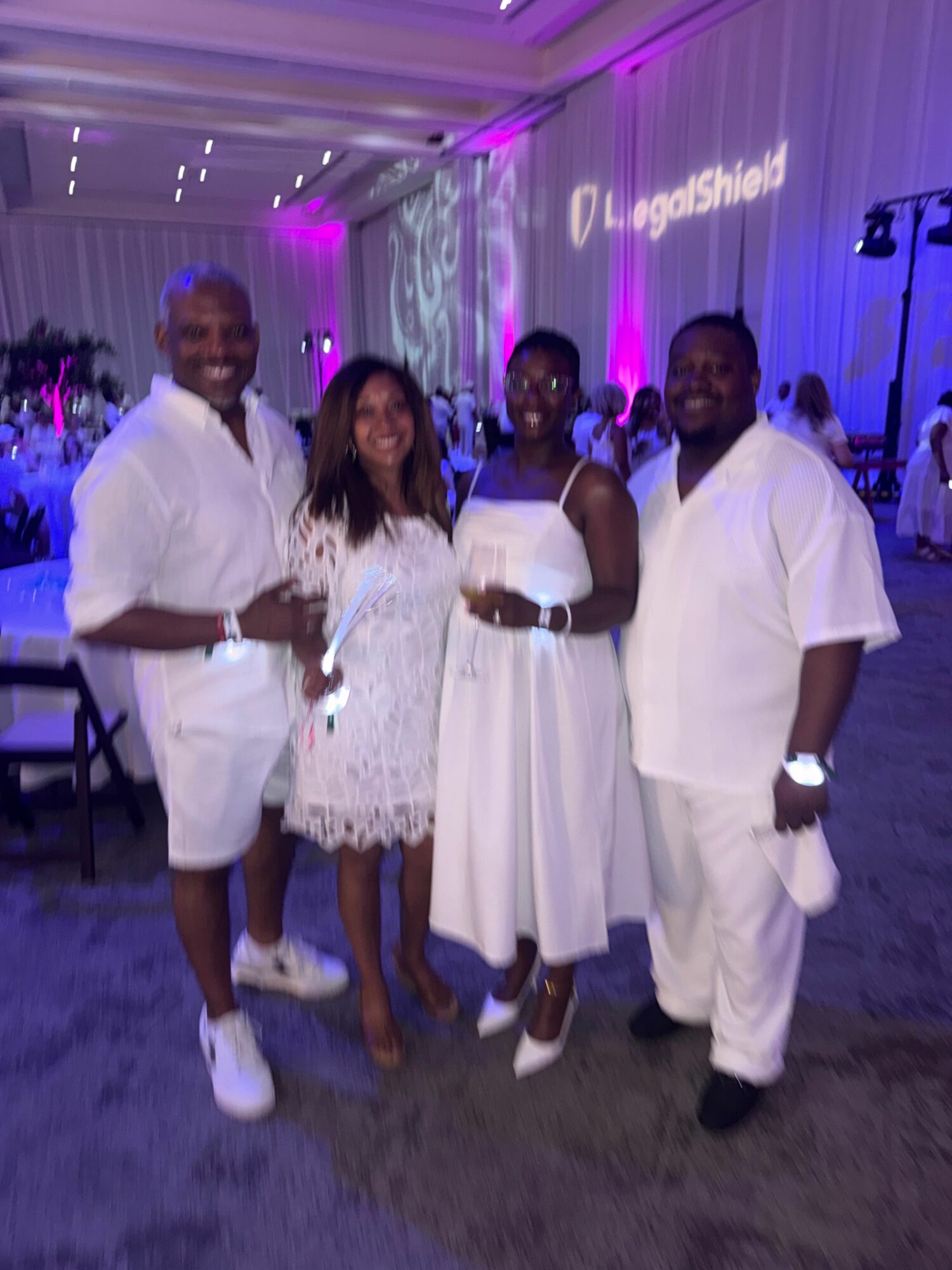 Four people standing together indoors, three men and one woman, with purple lighting and a decorated background.