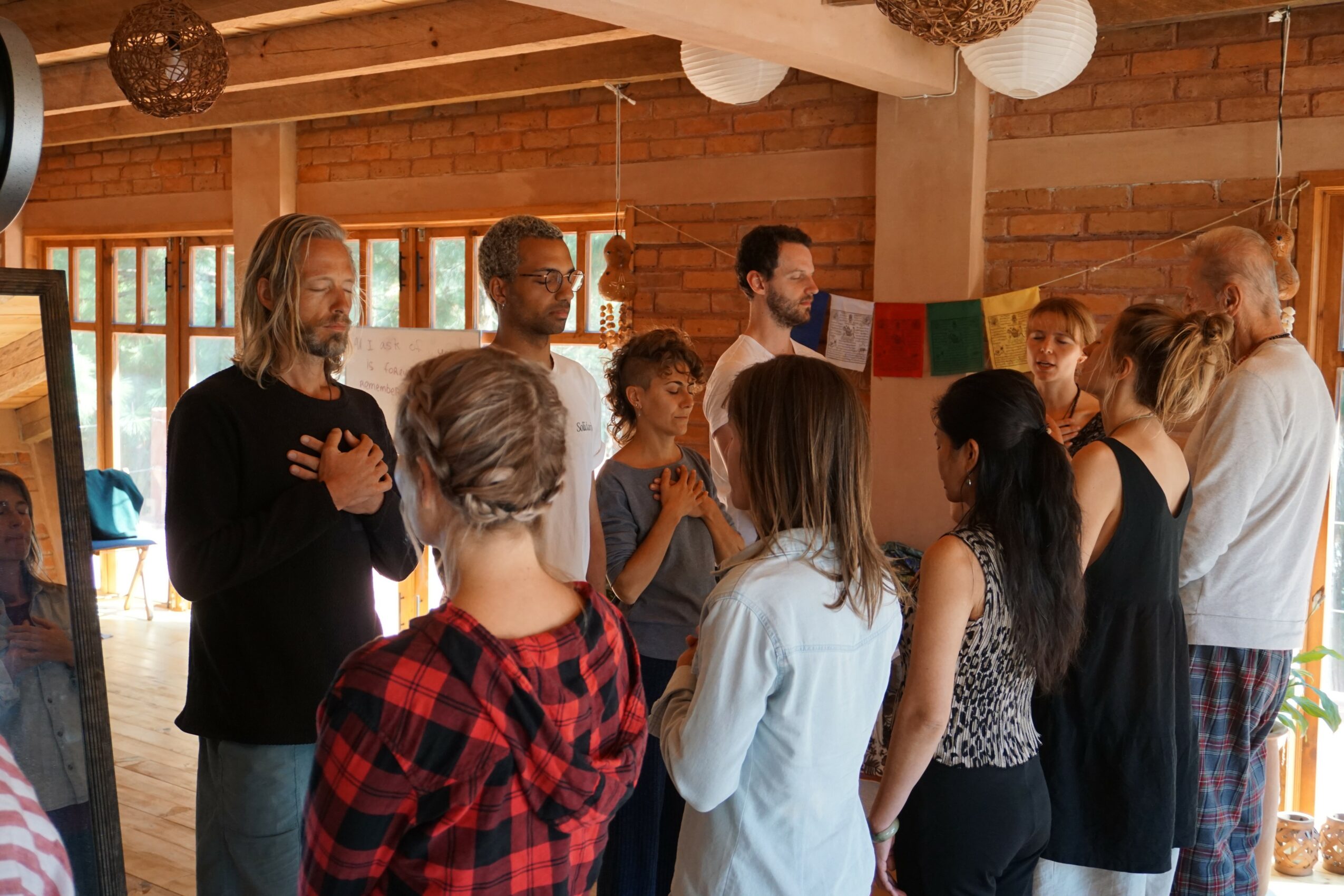 Group of people gathered indoors, some with hands over hearts, in a room with wooden walls and windows.