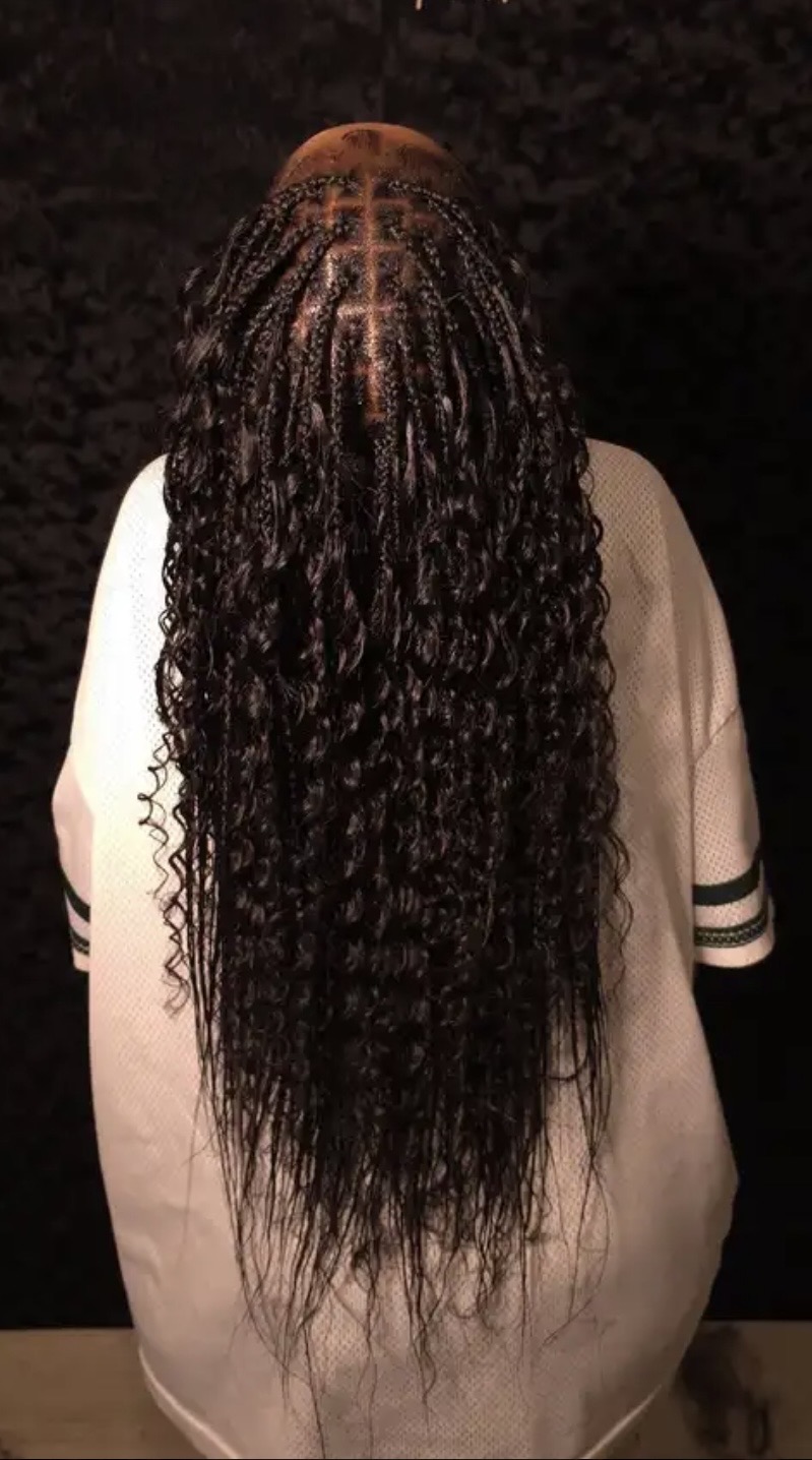 Person with long, curly hair seen from behind, wearing a white shirt with black stripes on sleeves.