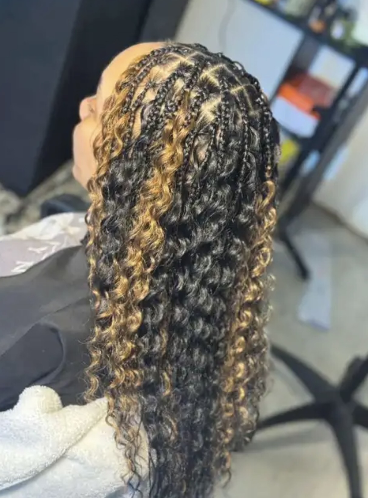 Person with long, curly hair featuring blonde highlights, viewed from the side in a salon setting.