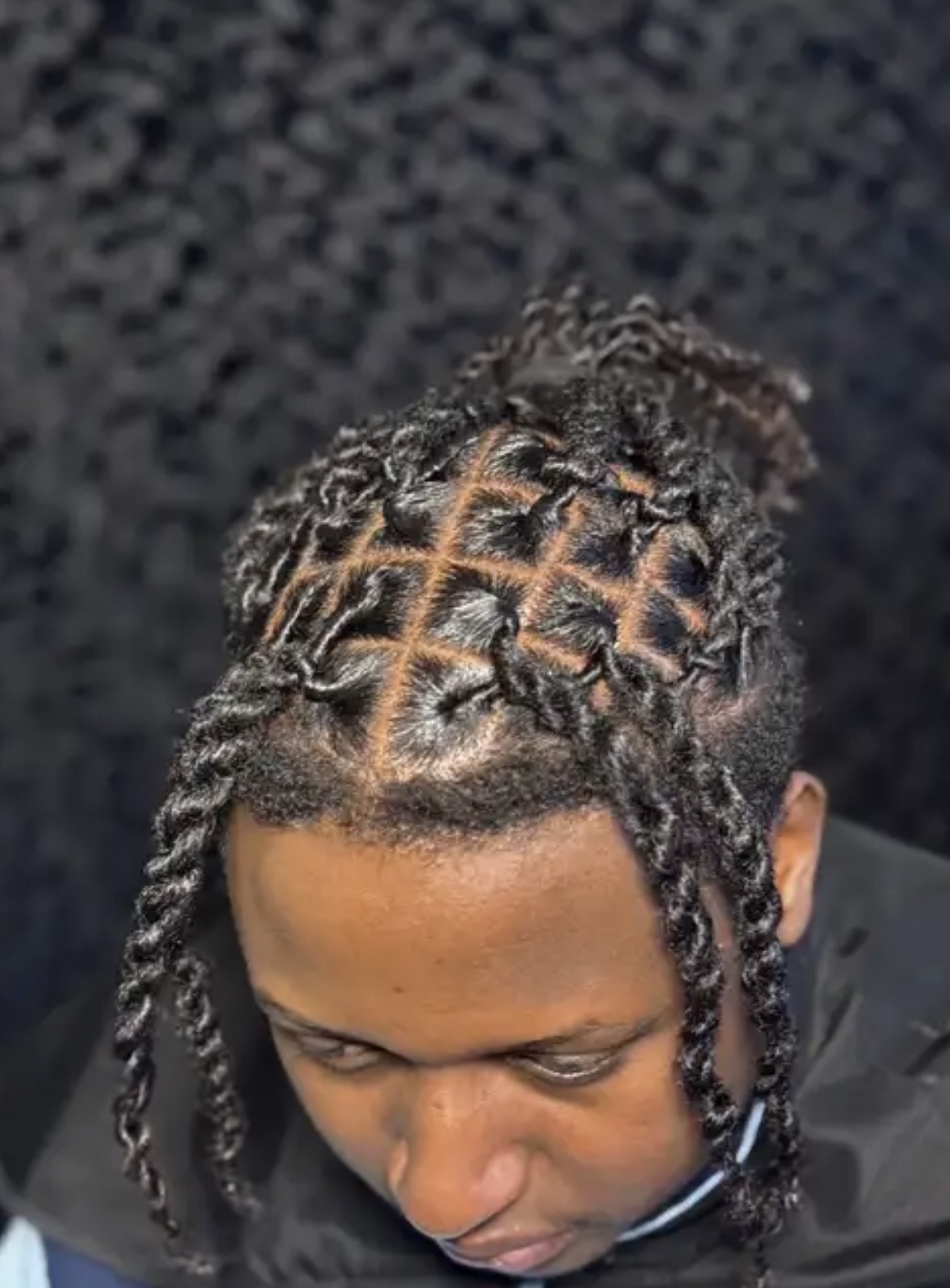 Top view of a person with styled dreadlocks, some tied in a pattern, against a dark background.