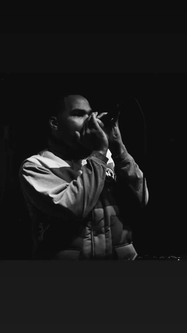 Person wearing sunglasses and a jacket, holding a camera or phone, in a dark setting.