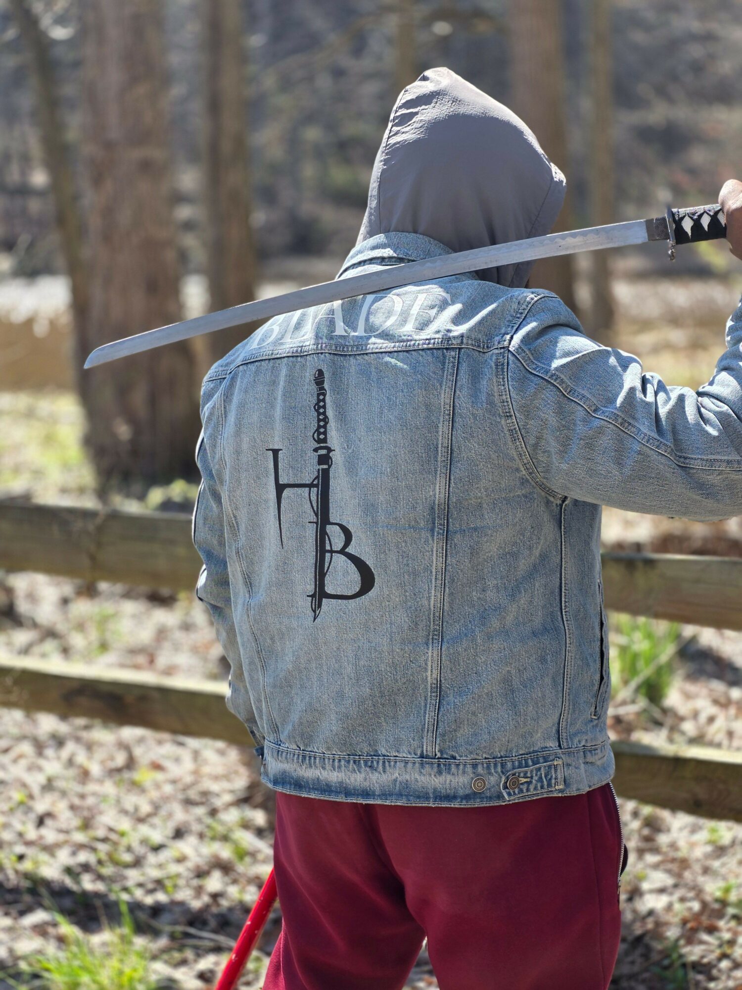 Person wearing a hoodie and jeans holding a golf club outdoors, with trees in the background.