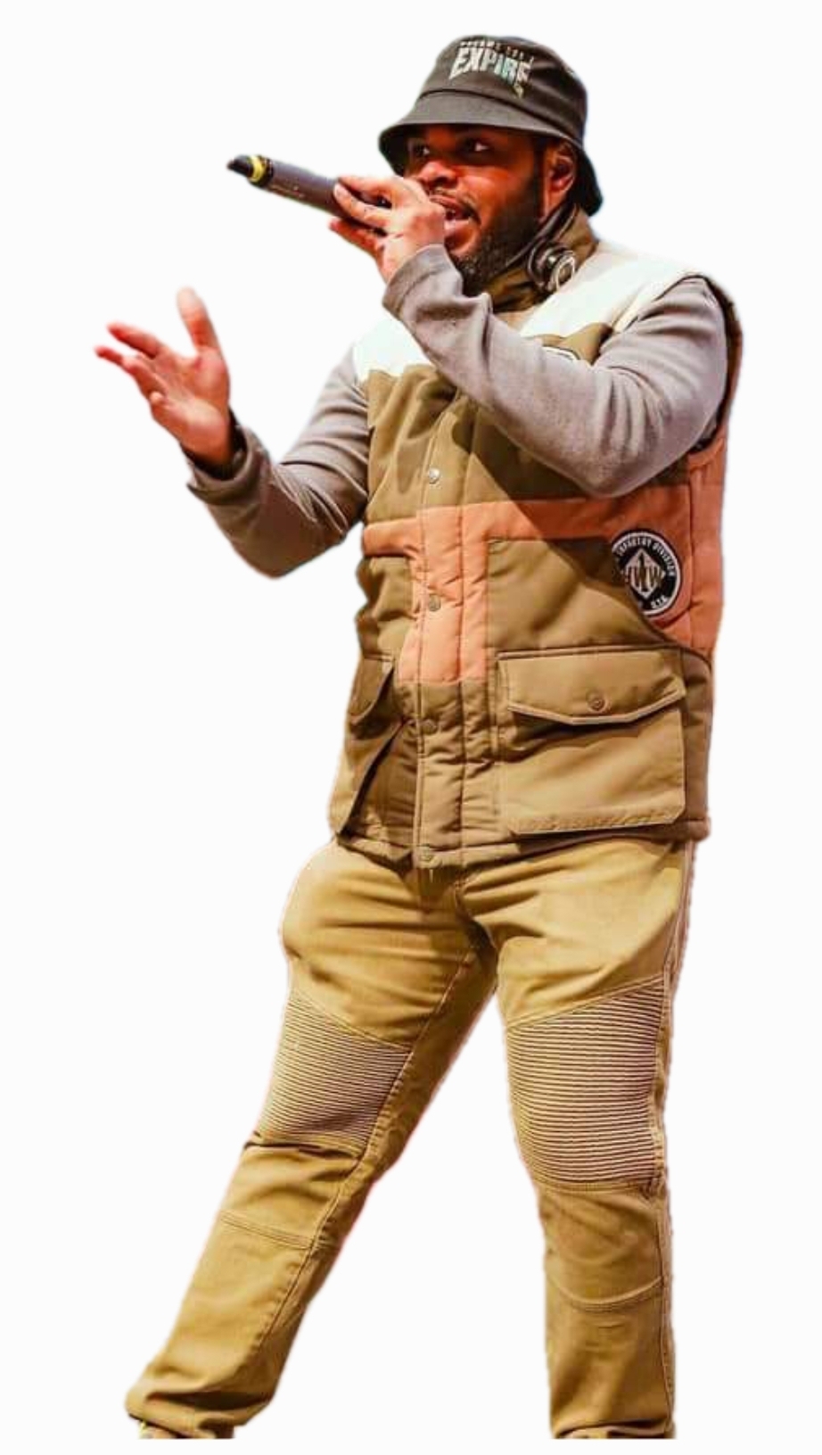 Person singing into microphone, wearing a bucket hat, beige vest, and pants, performing on stage.