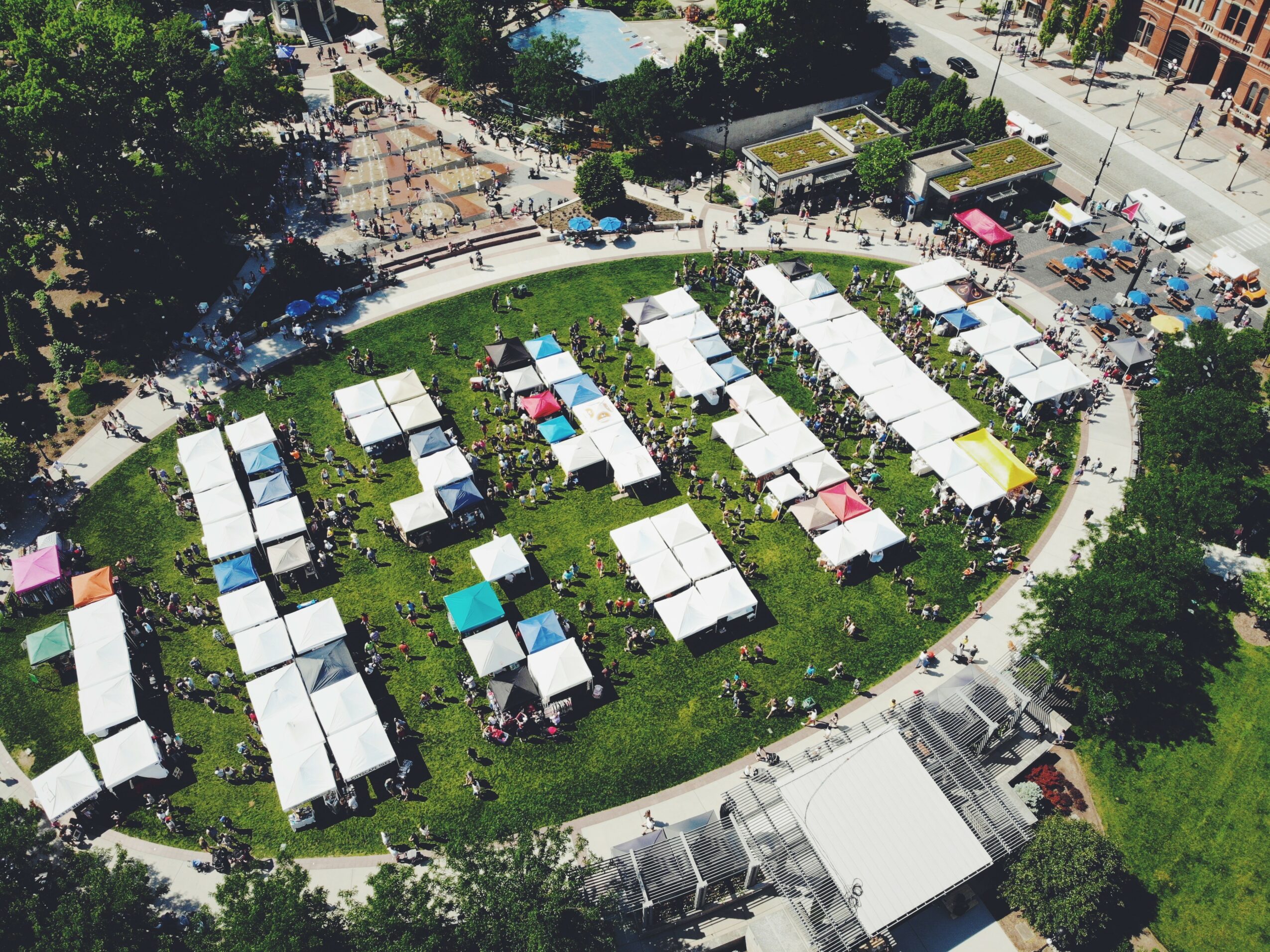Aerial view of a park with white tents arranged in a circular pattern, surrounded by trees and pathways.