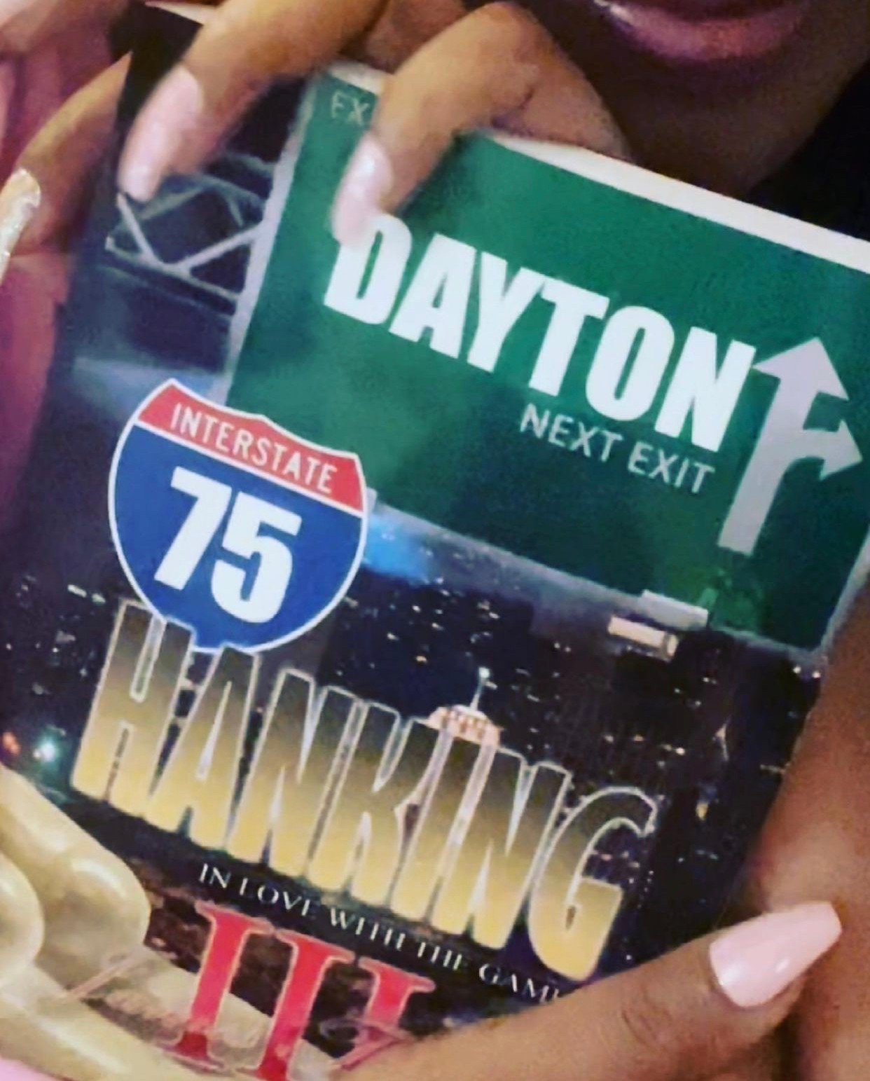 Person holding a sign for Dayton next exit and a book about Thanksgiving, with a cityscape background.