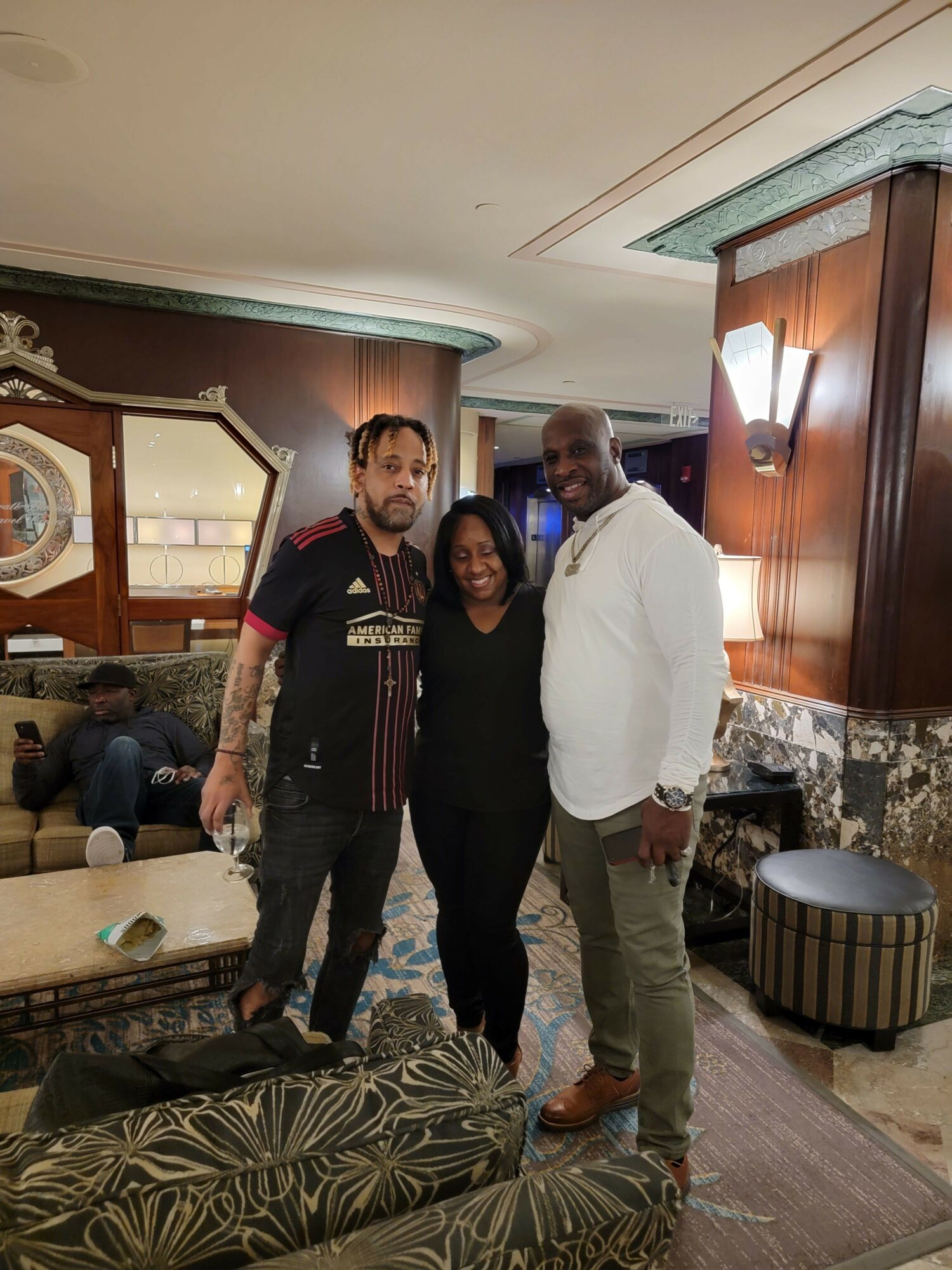 Four people standing in a room with wooden furniture and patterned carpet, posing for a photo.