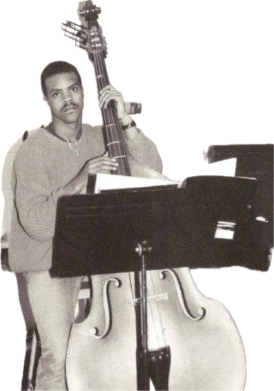 Person holding a double bass and standing behind a music stand, with a black background.