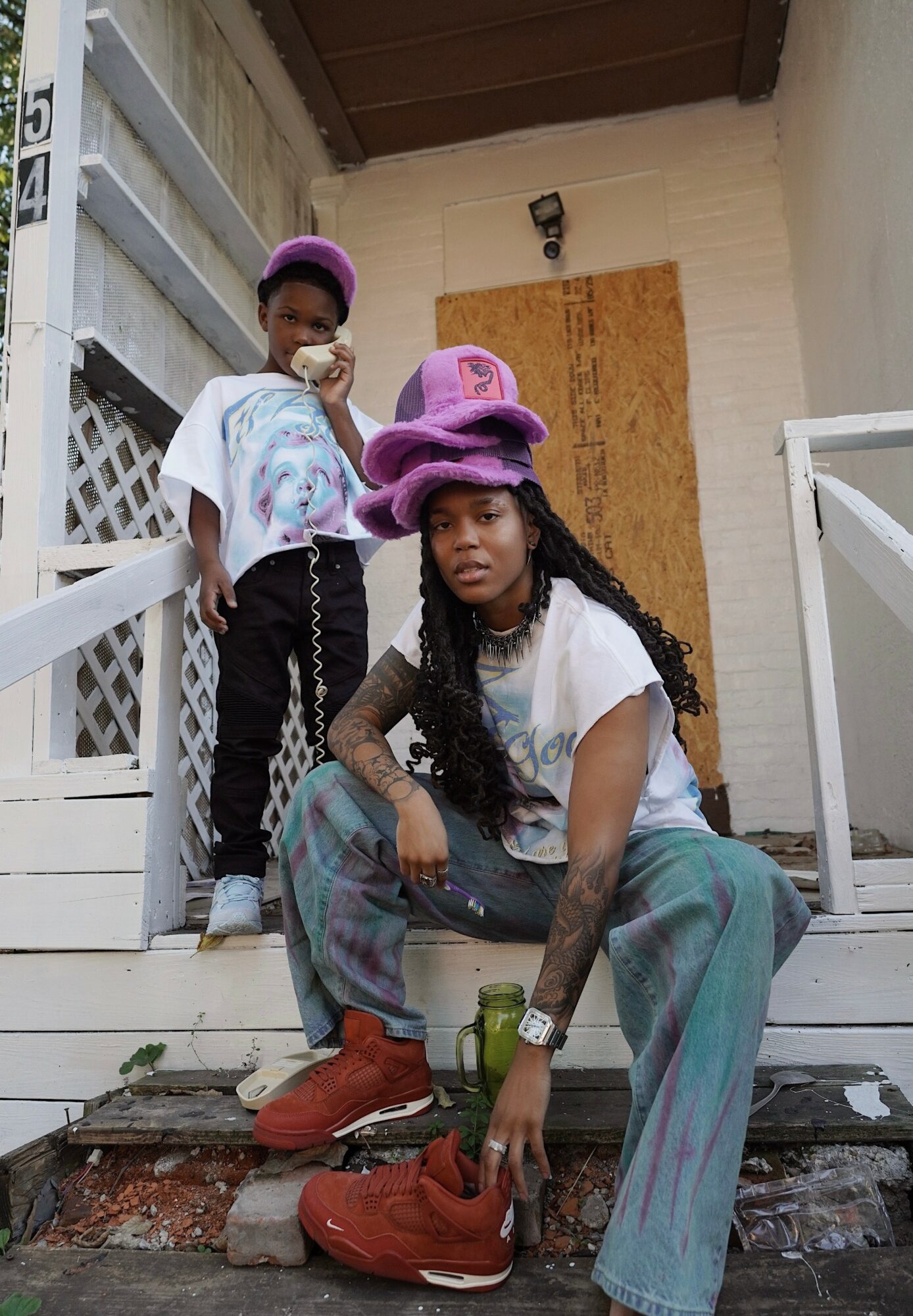 Two children with purple hats on front steps, one sitting and one standing, with a white railing and brick steps behind.