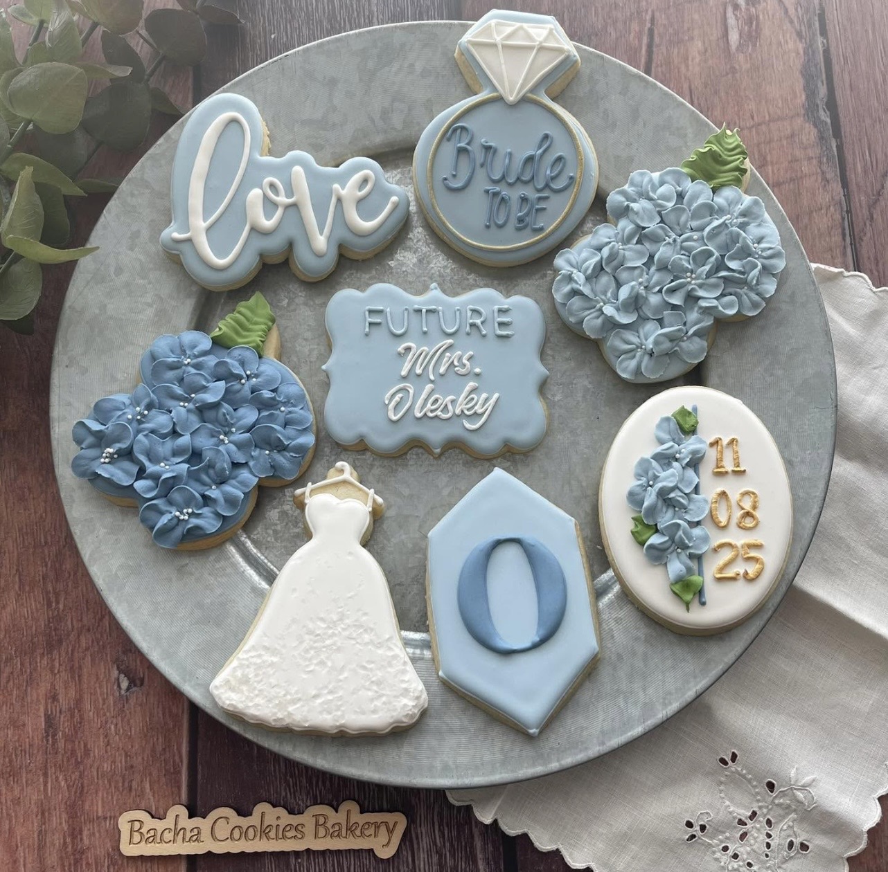 Collection of blue and white decorated cookies with love, diamond, wedding dress, and date designs on a gray plate.