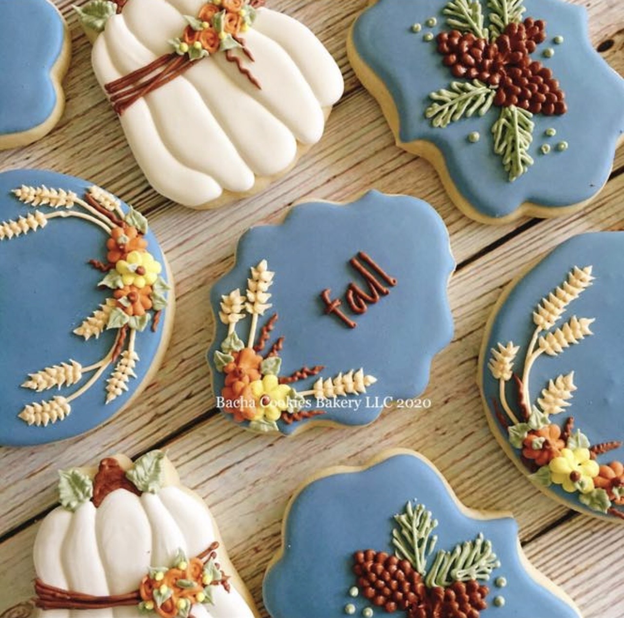 Decorated cookies with fall-themed designs, including pumpkins, leaves, and berries, on a wooden surface.
