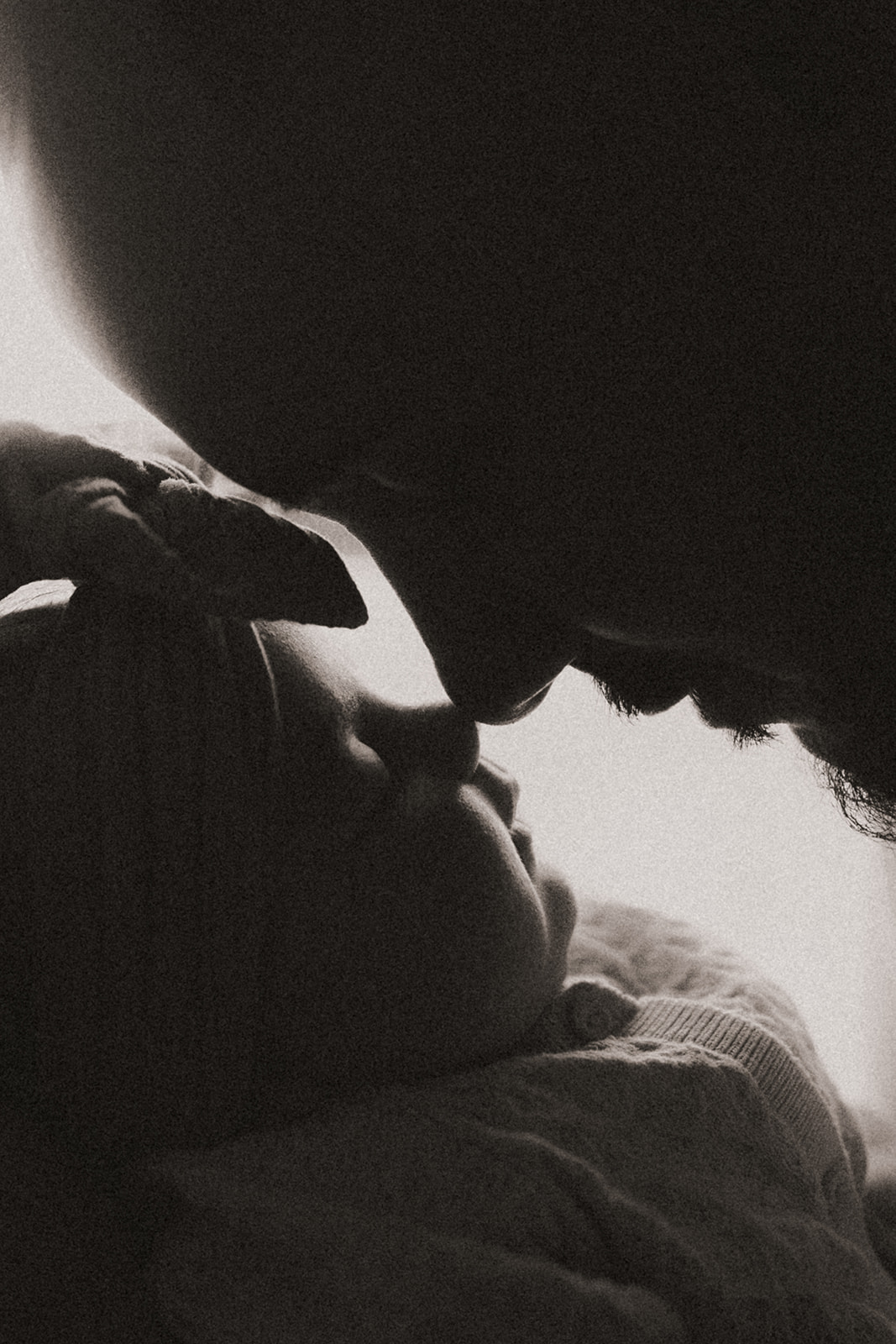 Person and baby close together, faces near each other, in black and white, intimate moment, soft lighting.