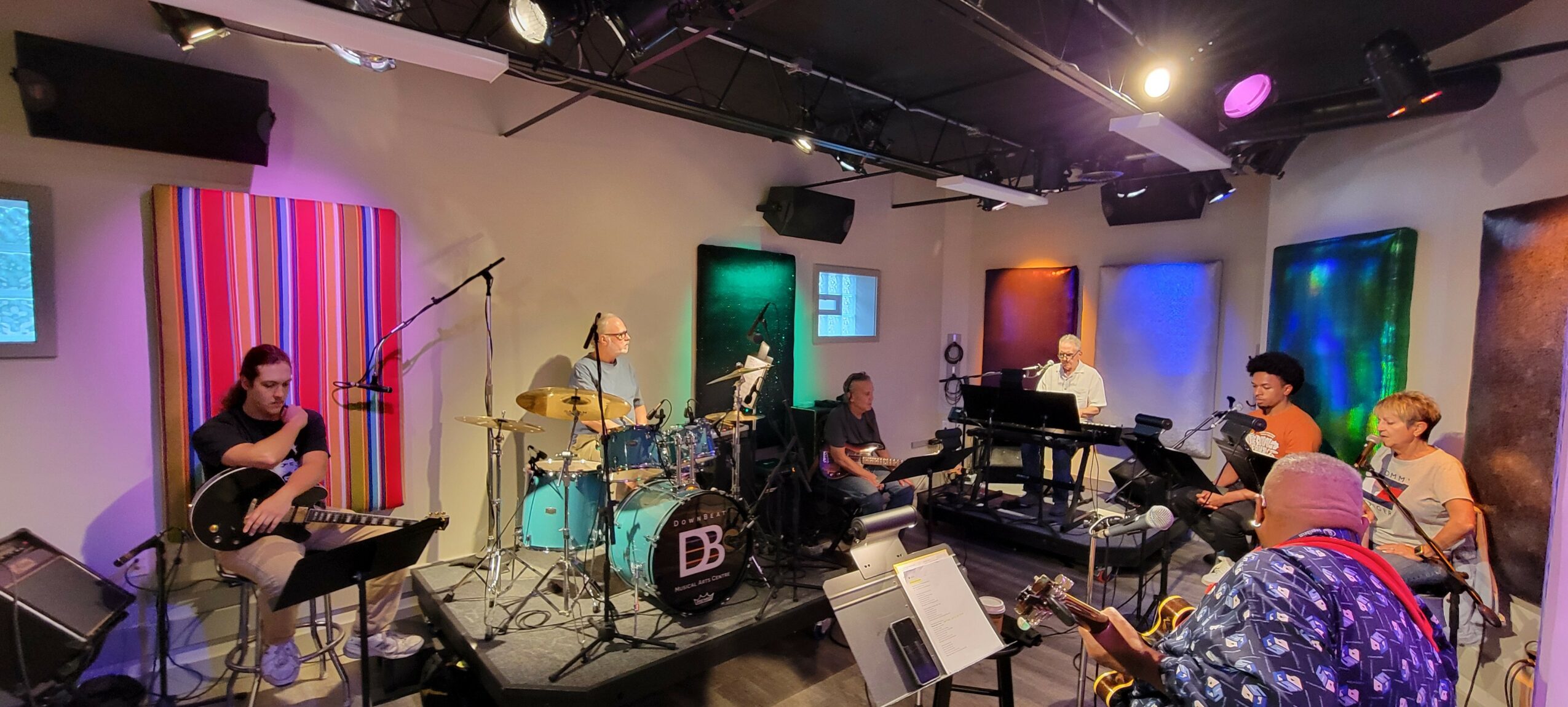 Group of musicians practicing in a studio with colorful wall art and musical instruments.