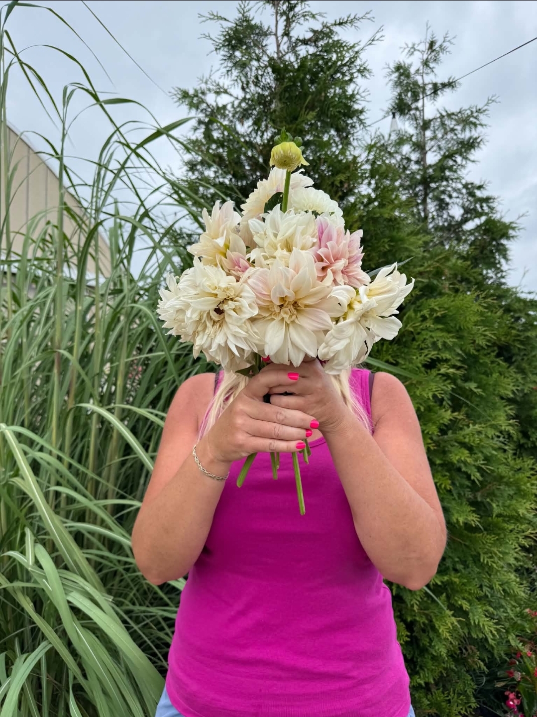 Person holding a large bouquet of white and pink flowers outdoors, with green trees and plants in the background.