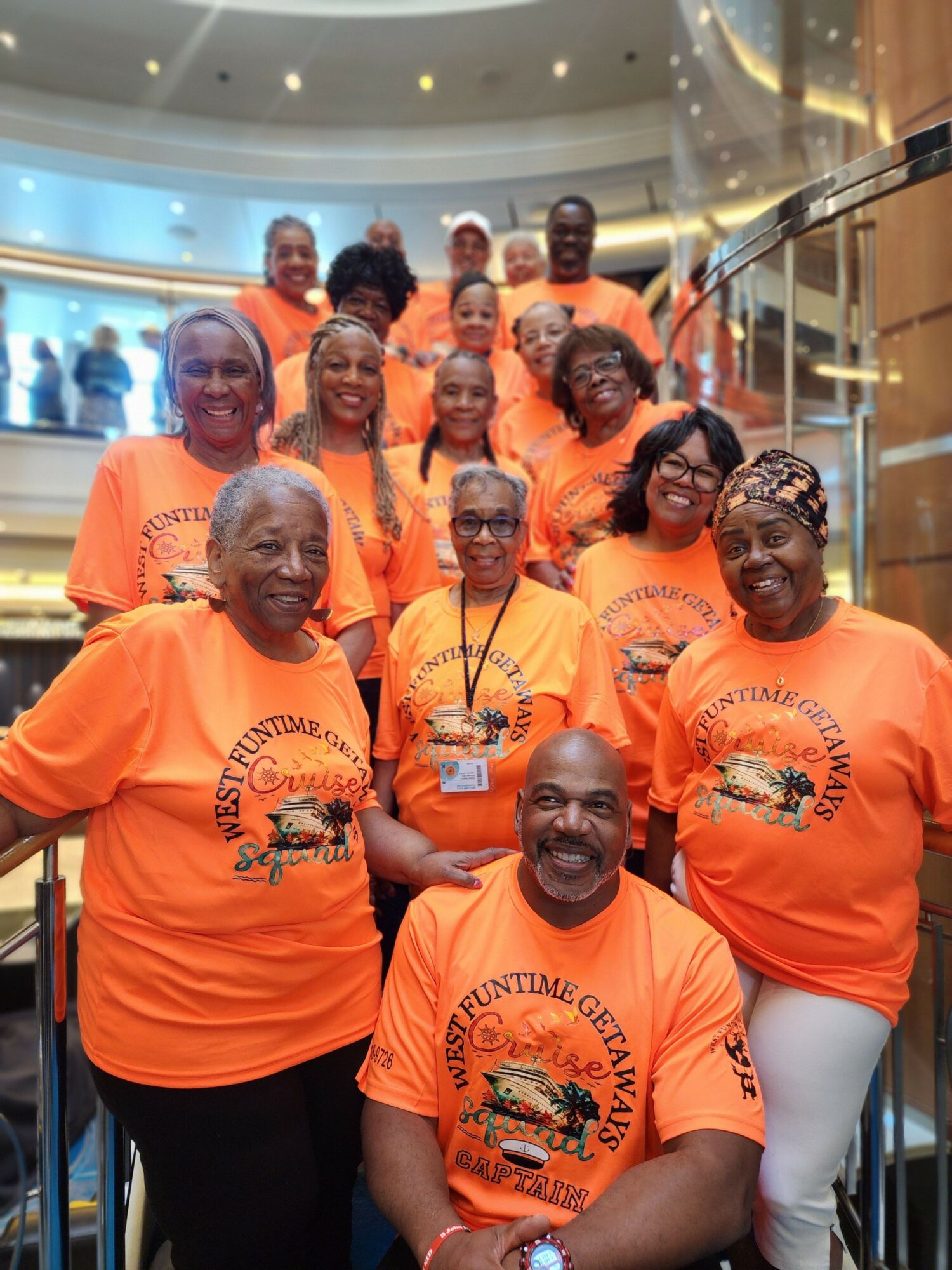 Group of people wearing matching orange shirts with a logo, smiling and posing together indoors.