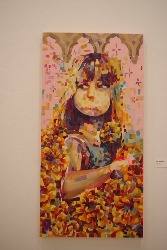 Pixelated portrait of a girl with dark hair, holding a phone, surrounded by orange flowers, against a pink background.